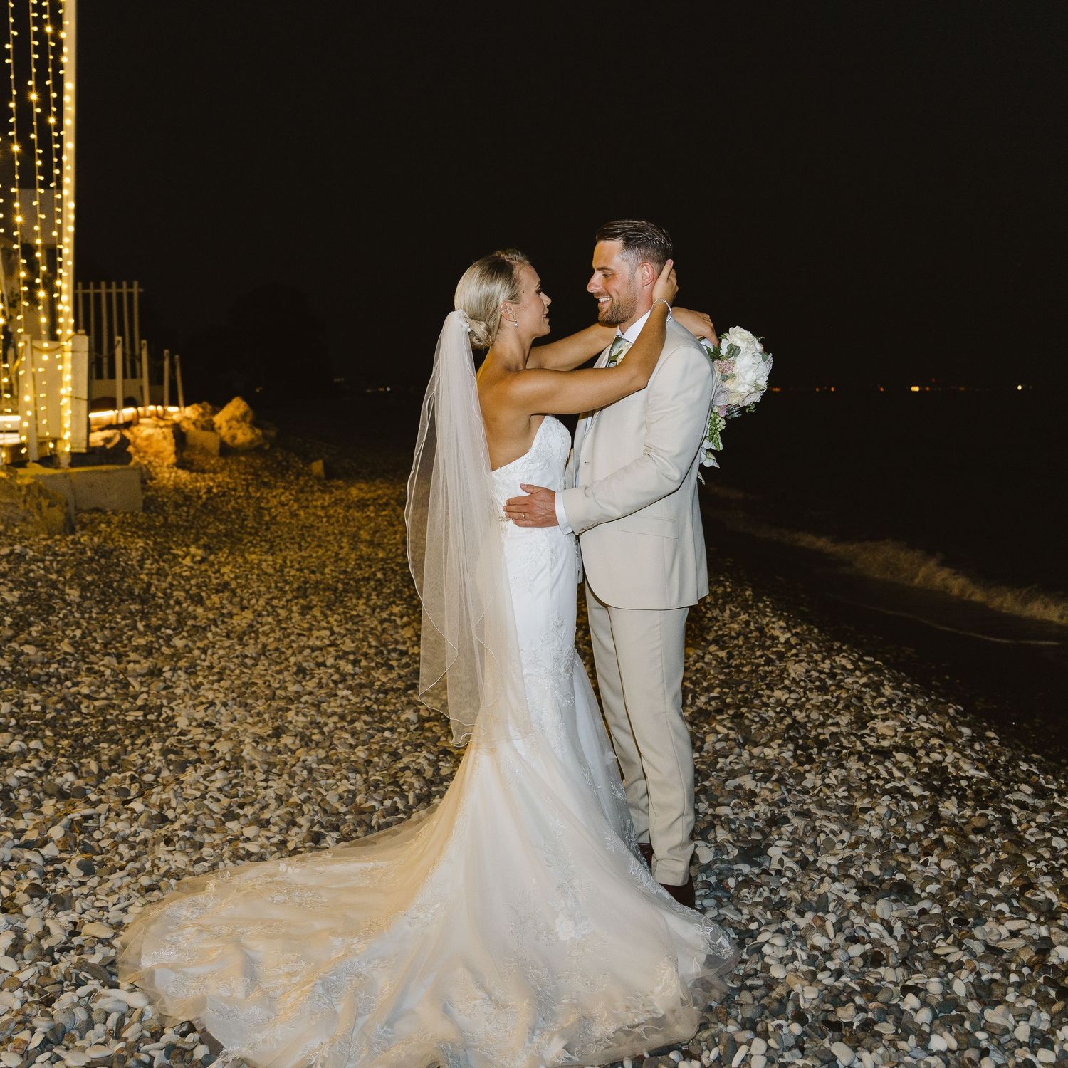 Romantic nighttime wedding portrait with twinkling lights in the background.