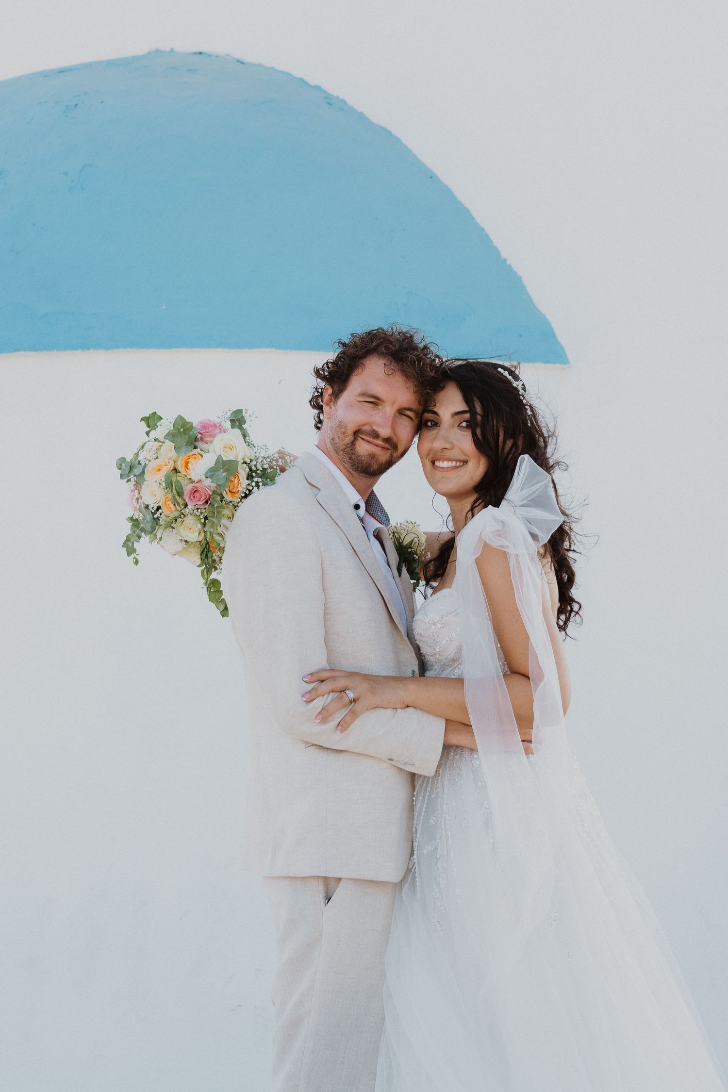 Intimate wedding portrait against white wall with bright blue accent in Mediterranean setting.