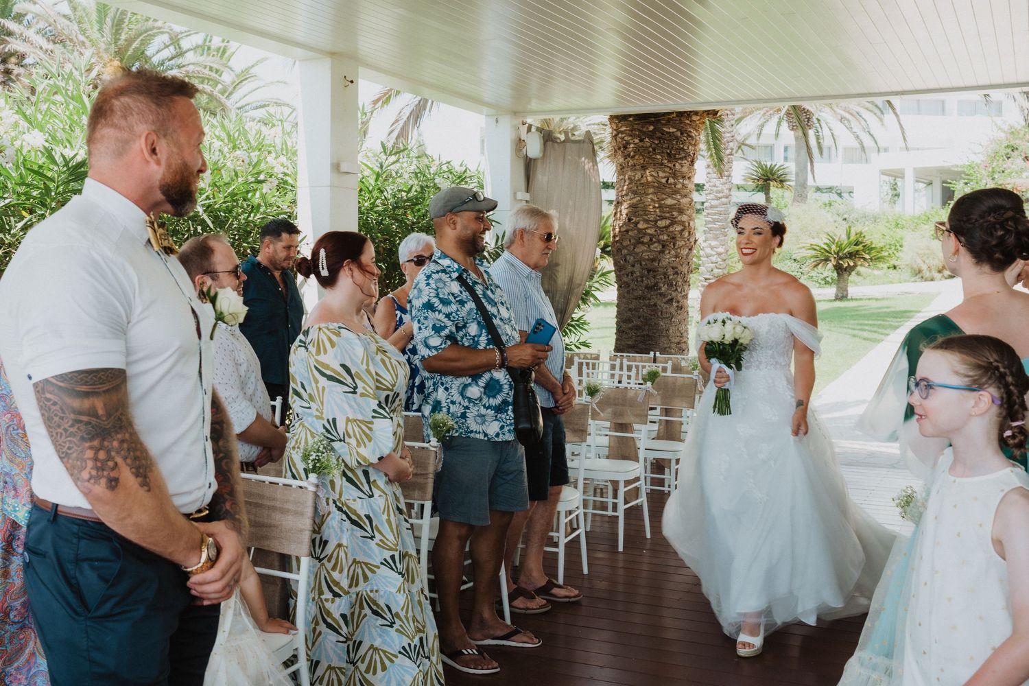 Wedding guests gather under a covered porch during an intimate outdoor ceremony.
