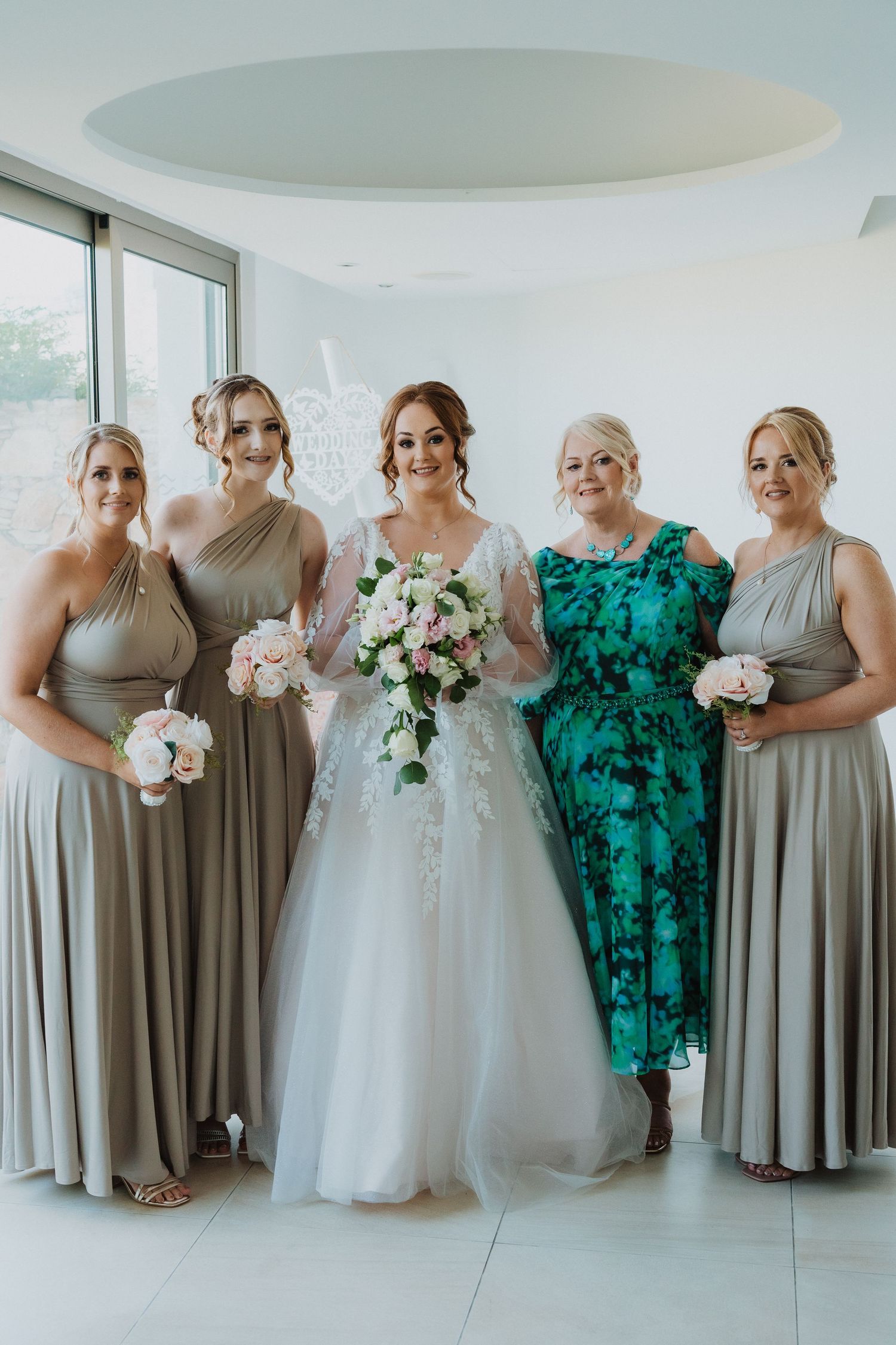 Wedding party wearing elegant gray bridesmaid dresses and one emerald green dress pose together with bouquets.