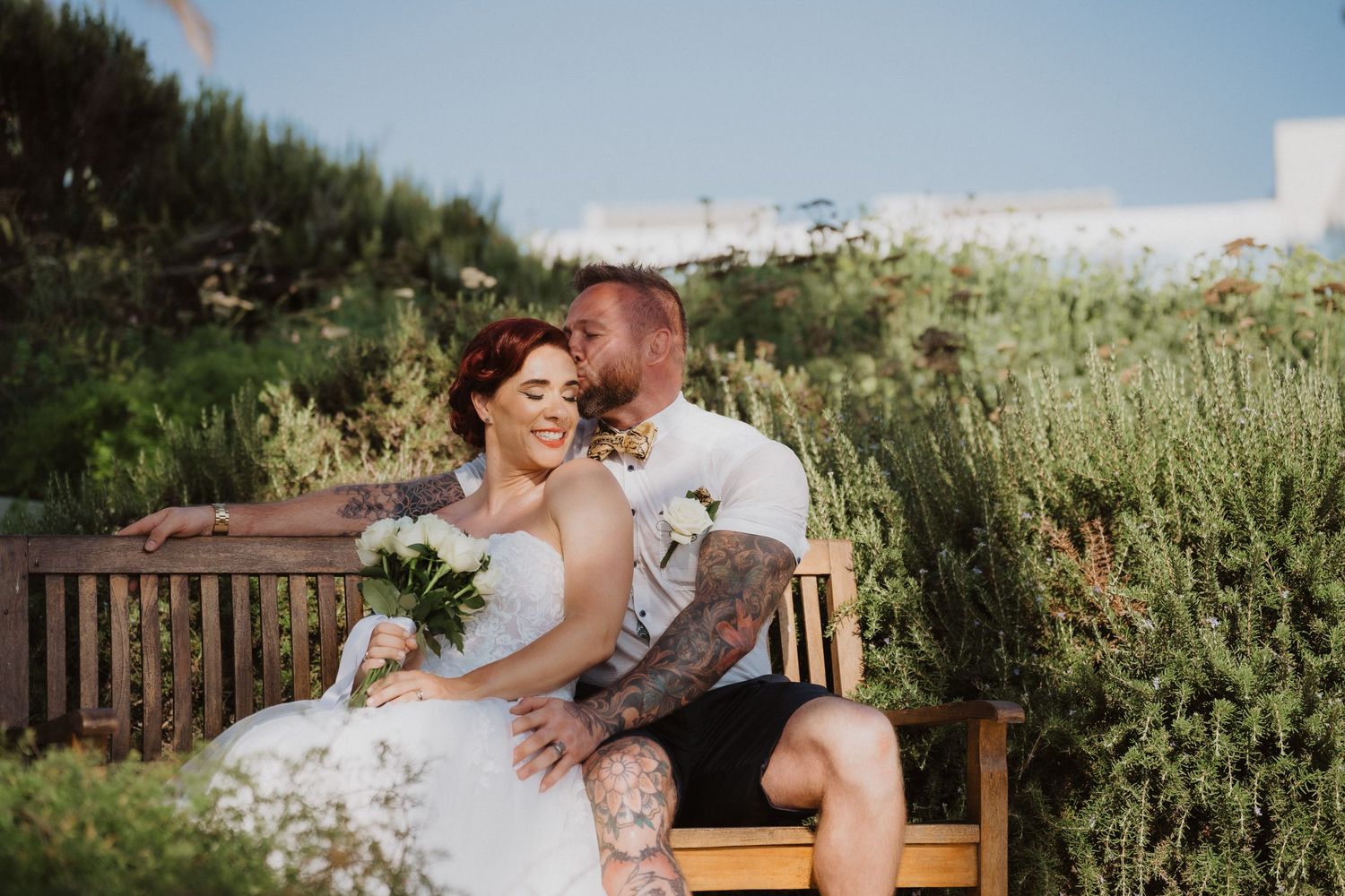 Couple shares intimate moment on wooden bench surrounded by lush greenery.