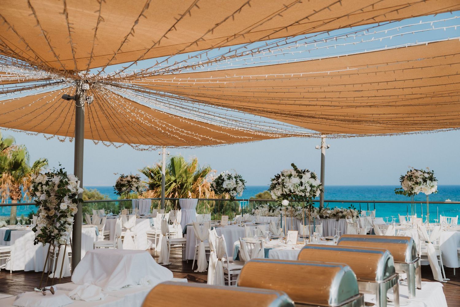 Elegant beachside wedding reception with white tables under a canopy, ocean views, and floral arrangements.