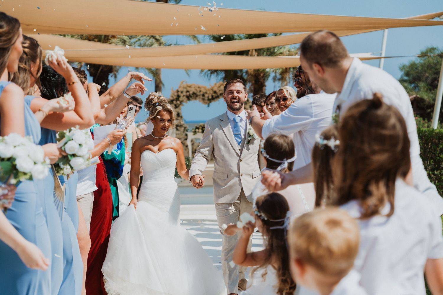 Joyful newlyweds walk down the aisle as guests shower them with confetti at an outdoor wedding ceremony.