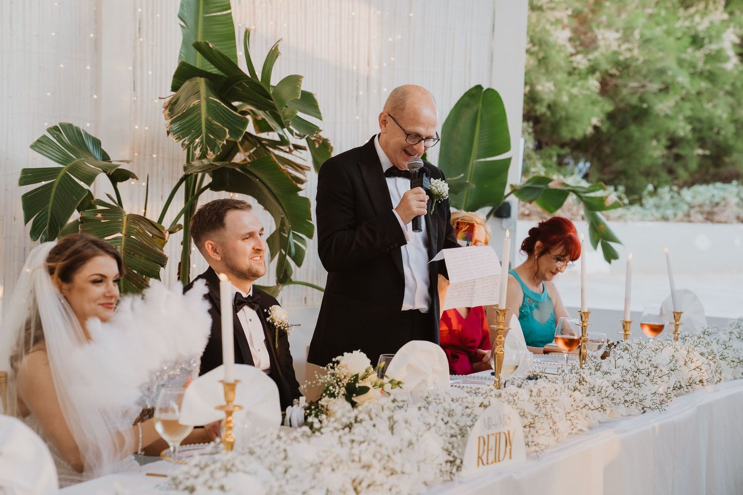 Wedding guest delivers a heartfelt speech at the head table decorated with white flowers and candles.