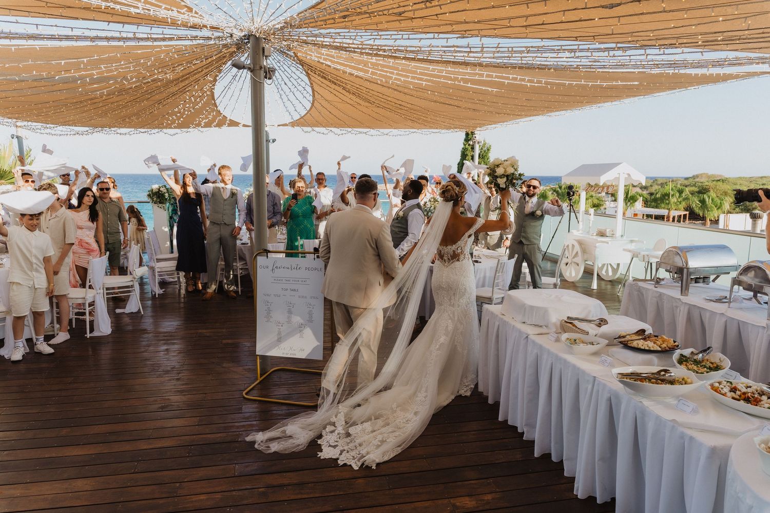 Wedding reception venue decorated with flowing beige fabric canopies and white table settings under a covered patio area.