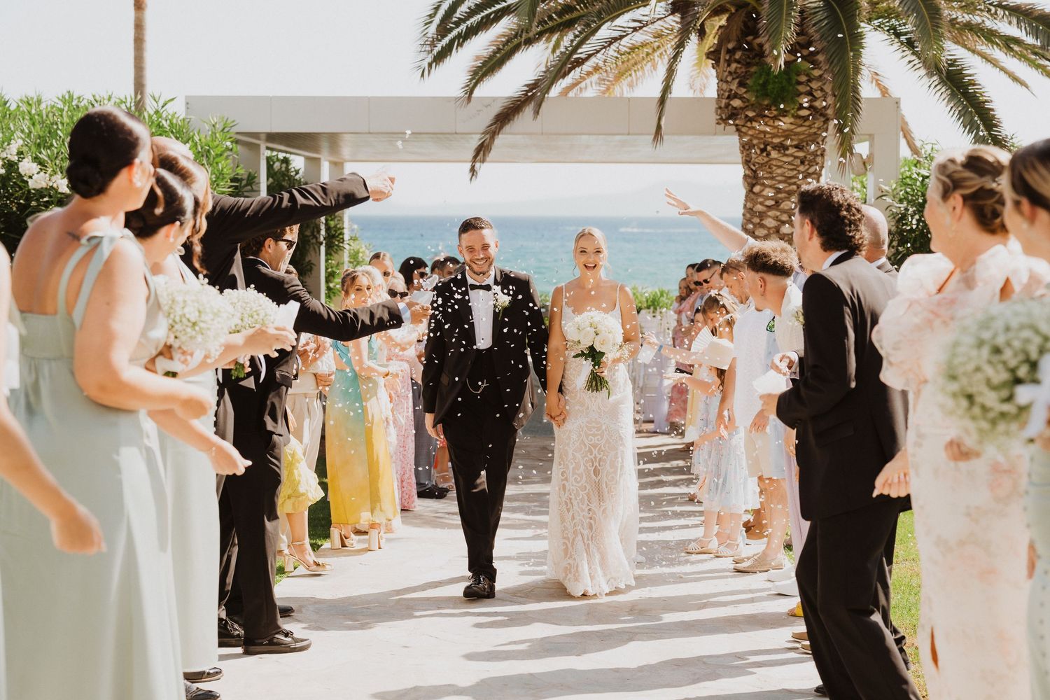 Wedding guests celebrate with confetti and champagne at an outdoor reception overlooking the ocean.