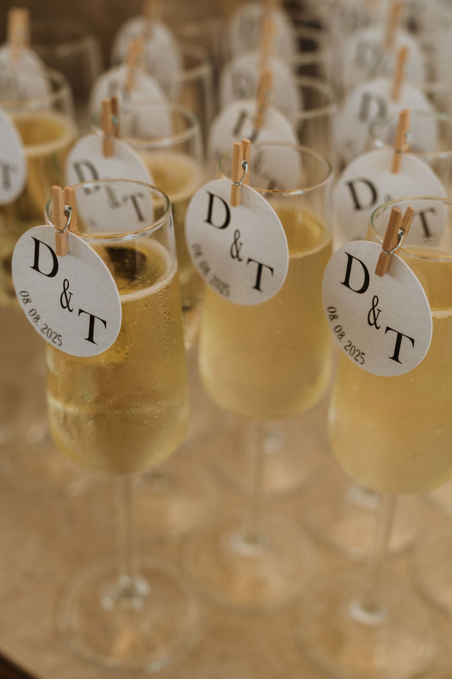 Wine glasses with hanging name tags labeled D&T arranged in a row at an elegant event setting.