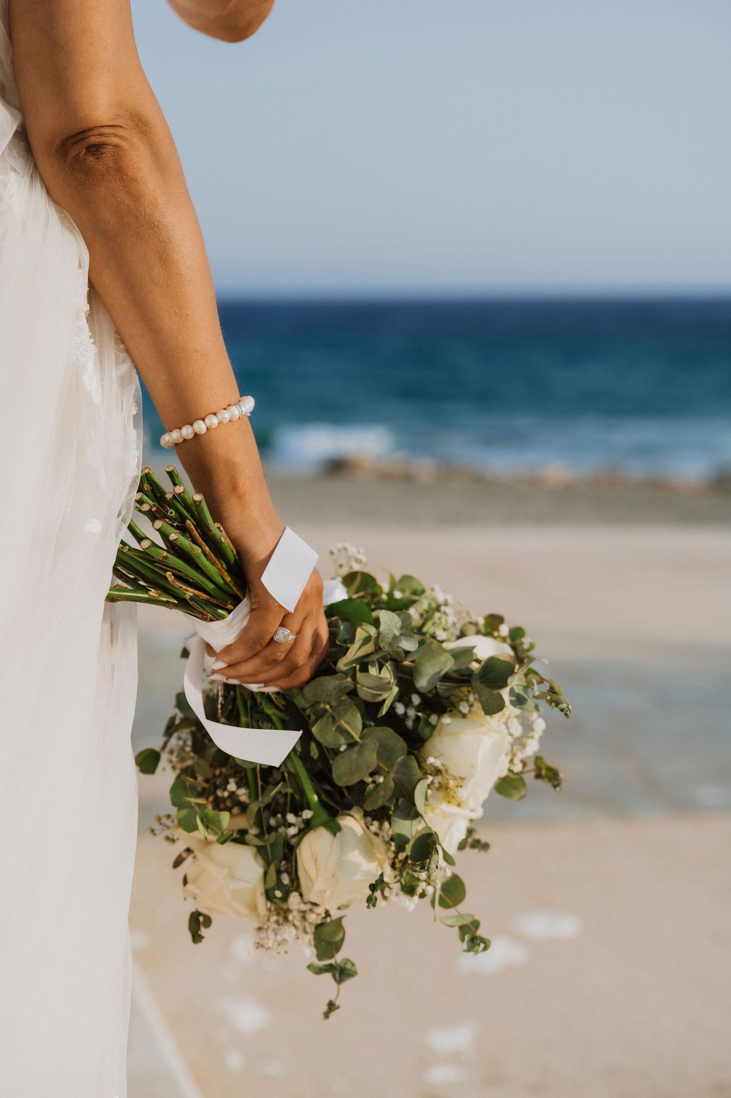 Close-up of a bridal bouquet with white flowers and greenery against an ocean backdrop.