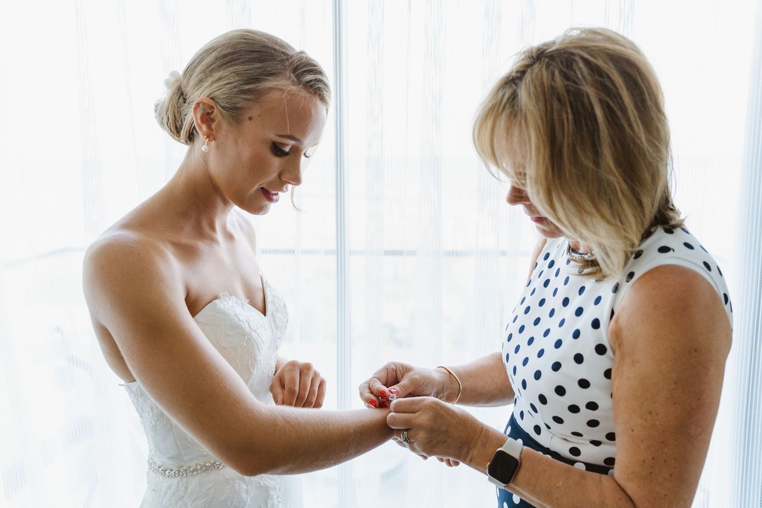 Final bridal preparations take place as accessories are adjusted in natural window light.
