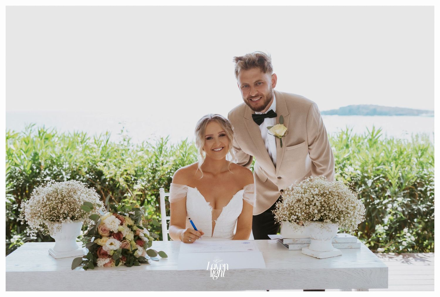Wedding couple at signing table decorated with baby's breath floral arrangements.