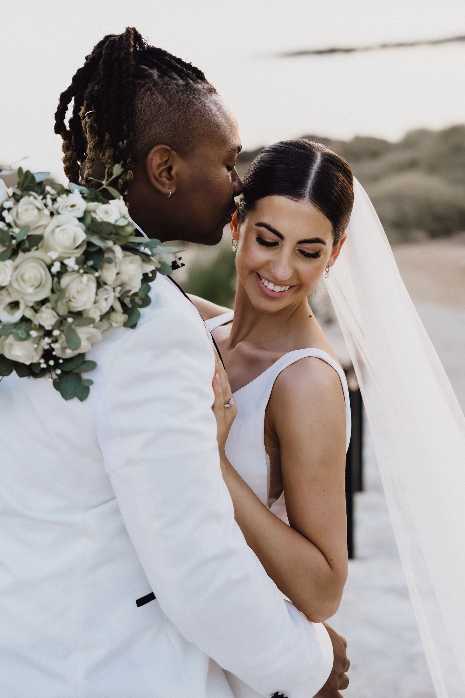 Intimate wedding moment captured with white roses bouquet against coastal Mediterranean backdrop.