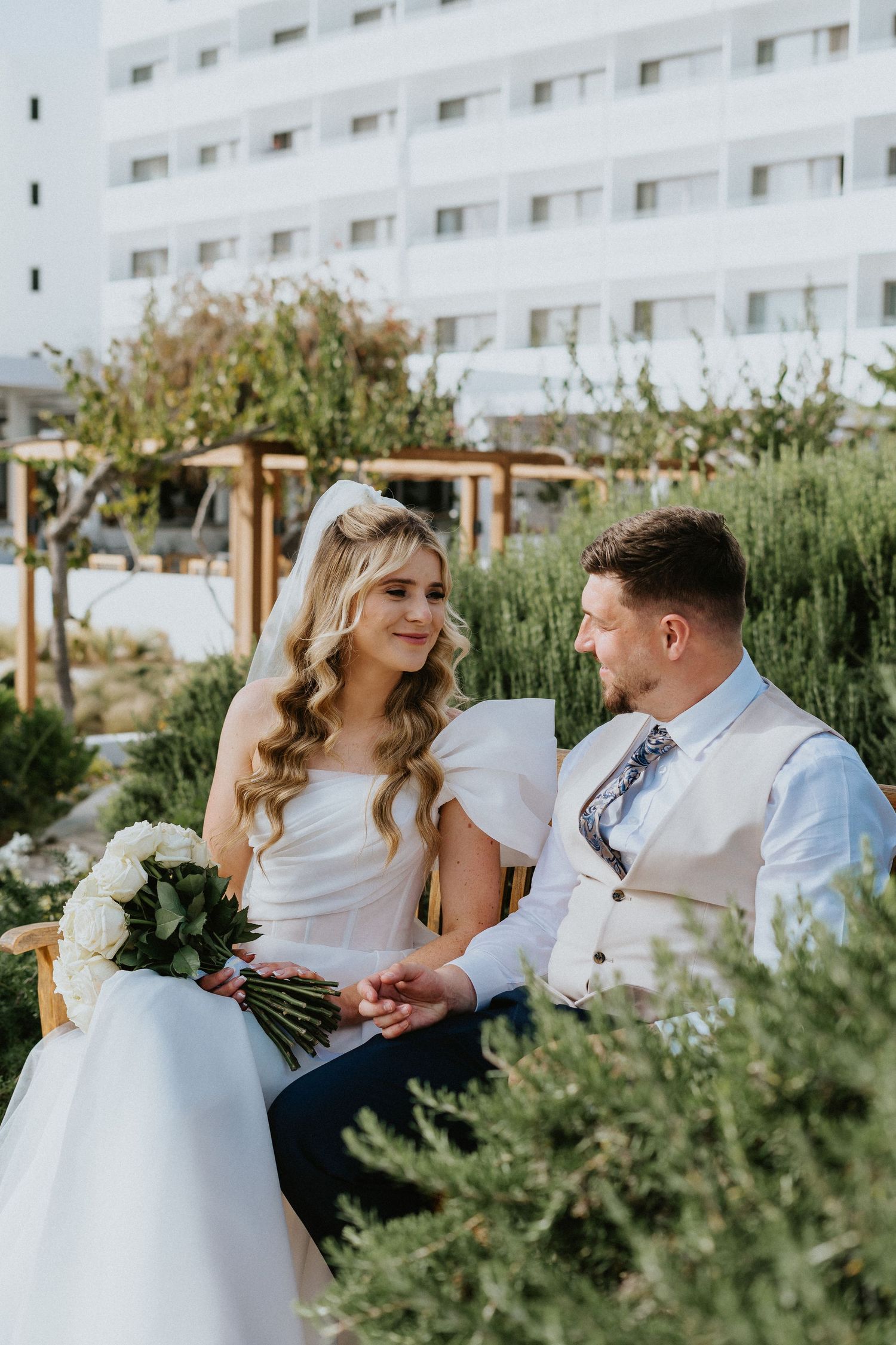 Garden wedding portrait with white bouquet and modern building backdrop.