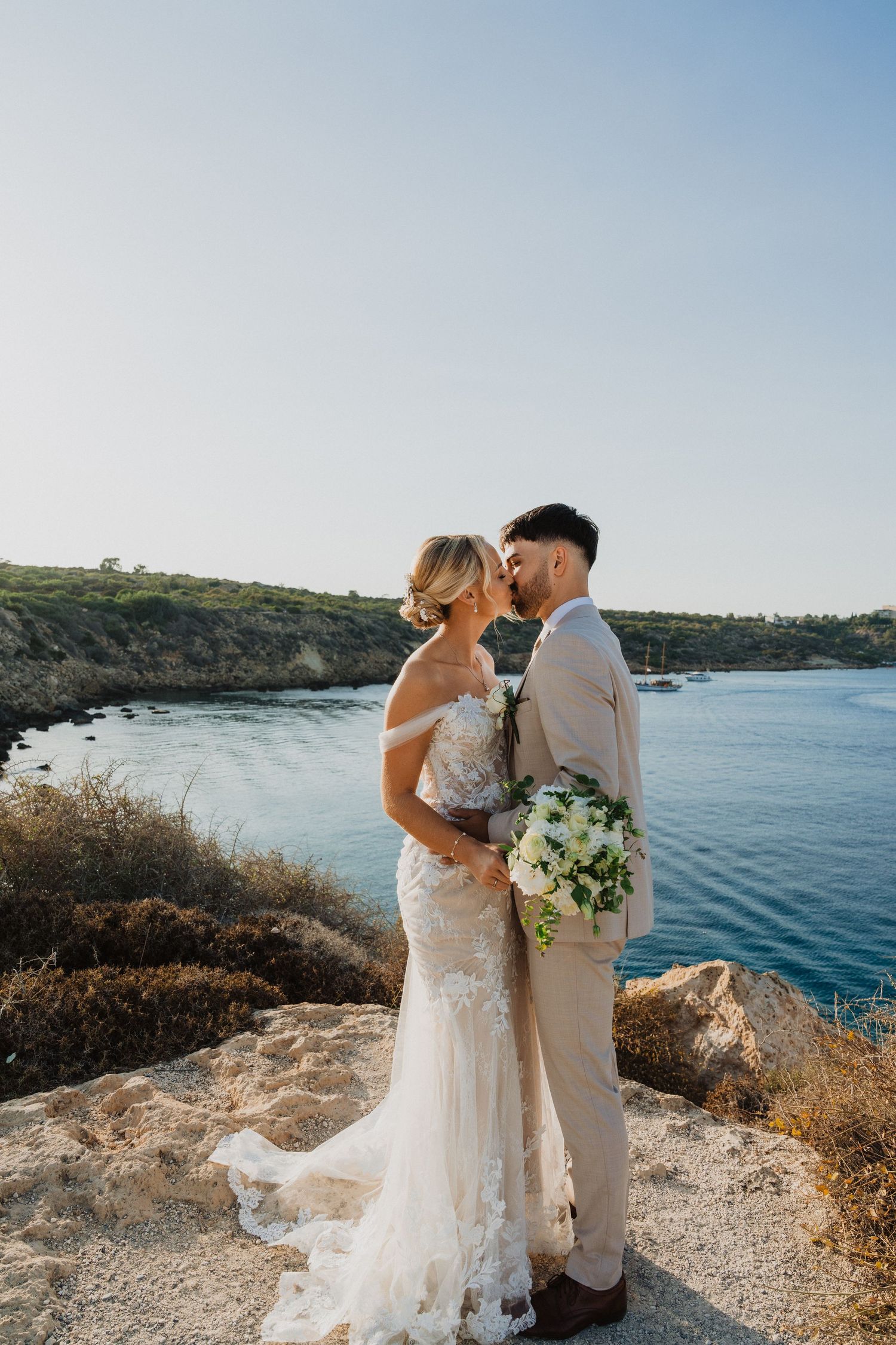 Romantic wedding photo on coastal cliff overlooking calm blue waters.
