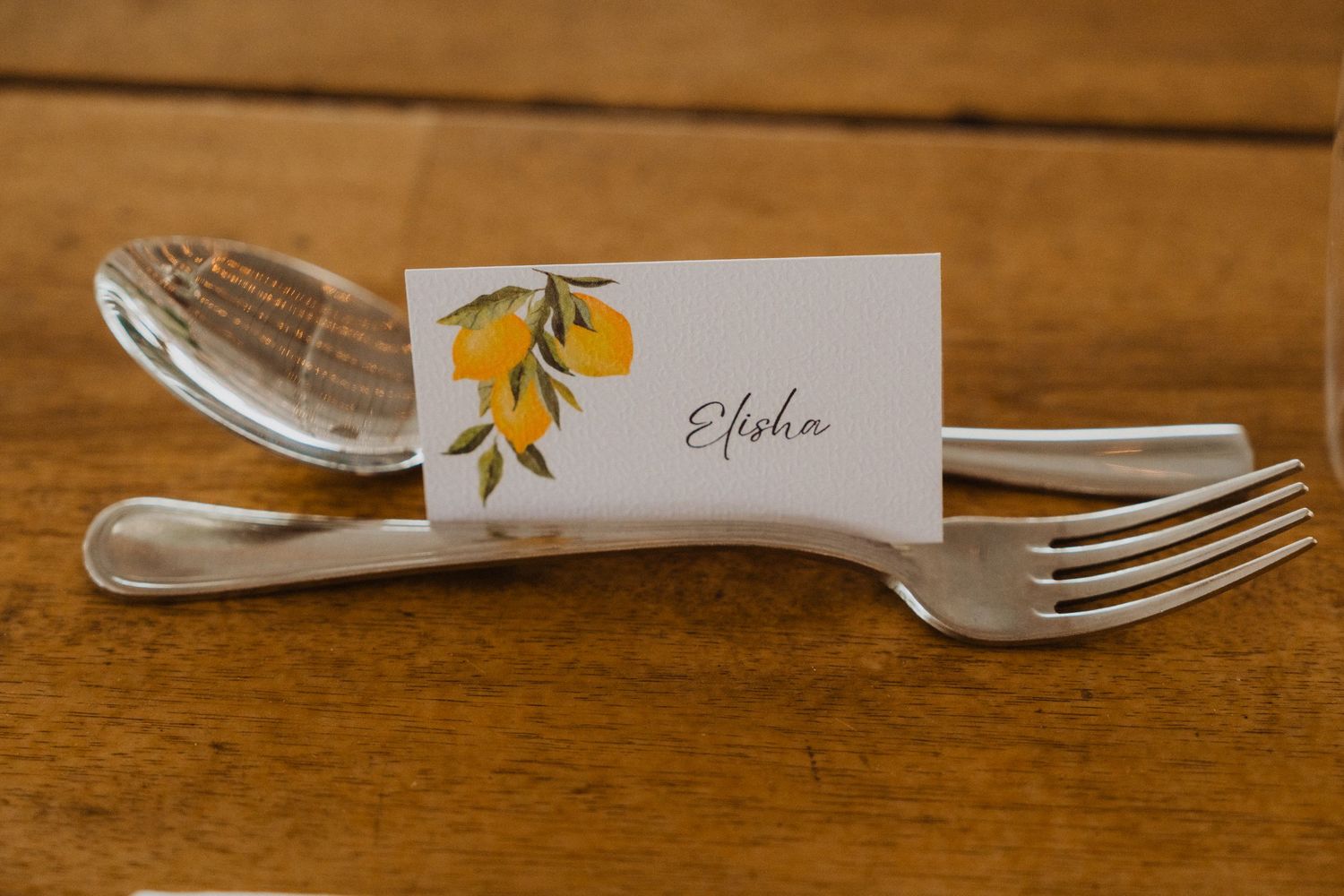 Close-up of place settings with citrus-themed name cards and silverware on wooden tables.