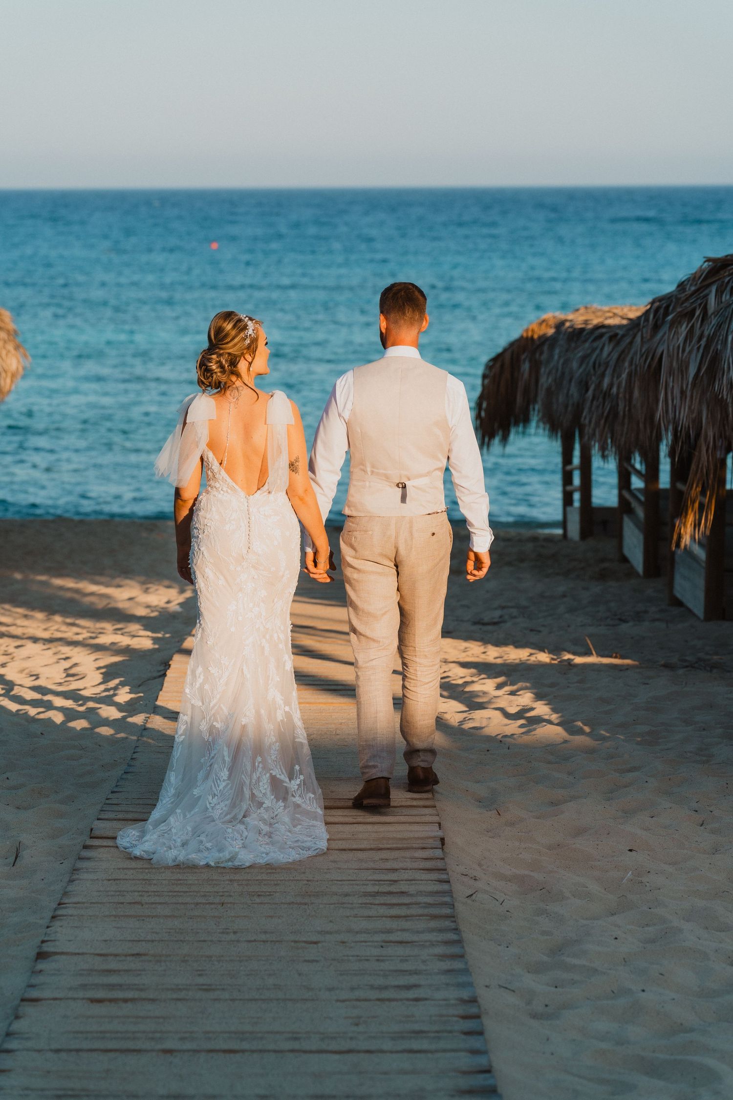 Couple walking on wooden boardwalk at beach during sunset.