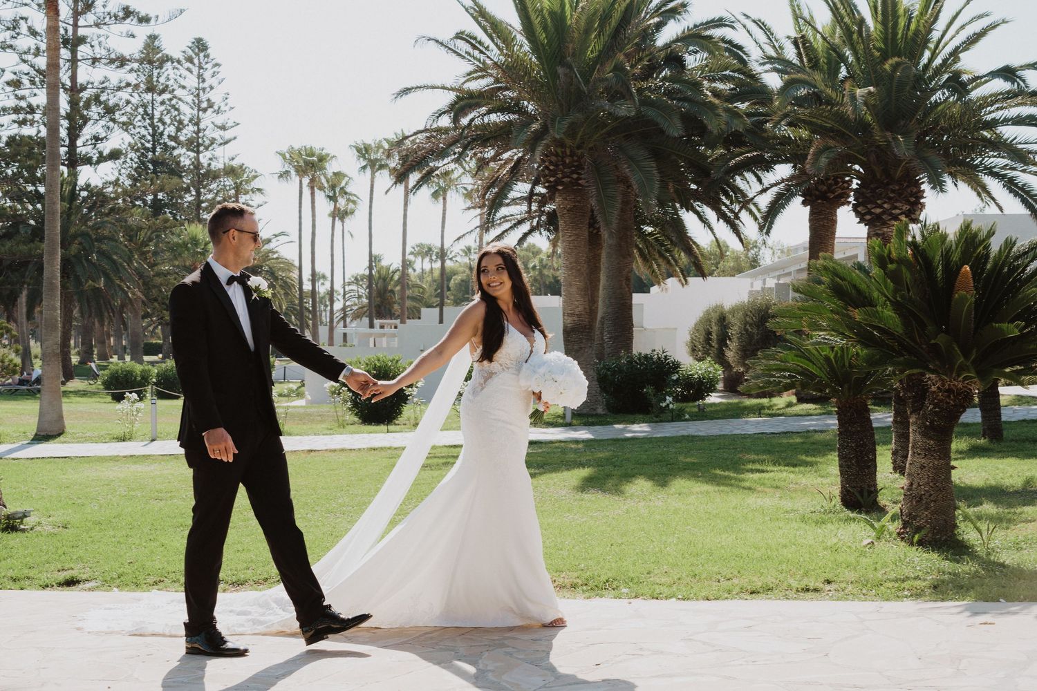 A couple walks along a palm-lined path during their tropical beach wedding celebration.