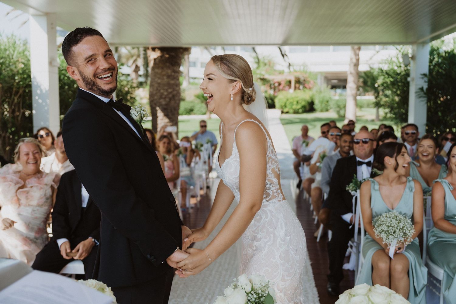Couple shares joyful moment during wedding ceremony under white covered pavilion.