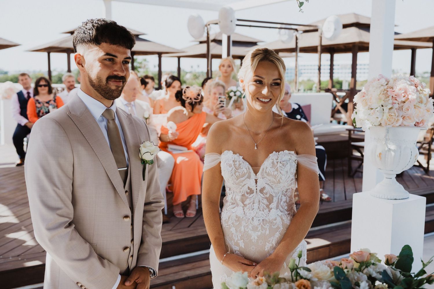 A couple exchanges vows during their beach wedding ceremony under floral decorations.
