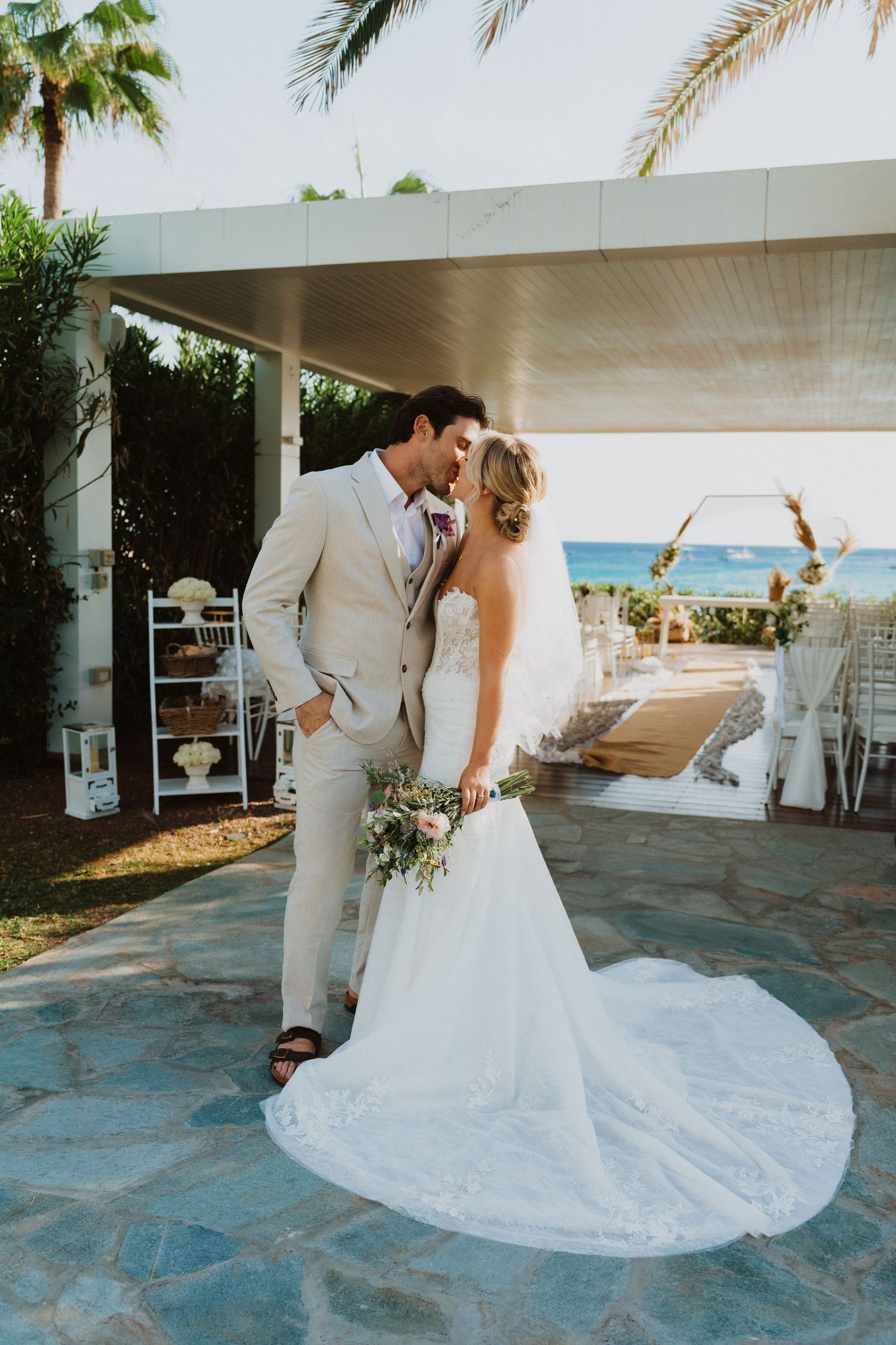 Wedding couple poses for romantic photos on a blue stone patio with palm trees and ocean backdrop.