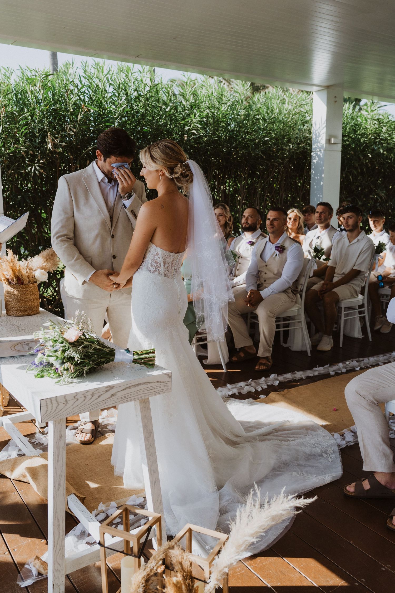 Wedding party members in white and beige attire gather at an outdoor covered venue.