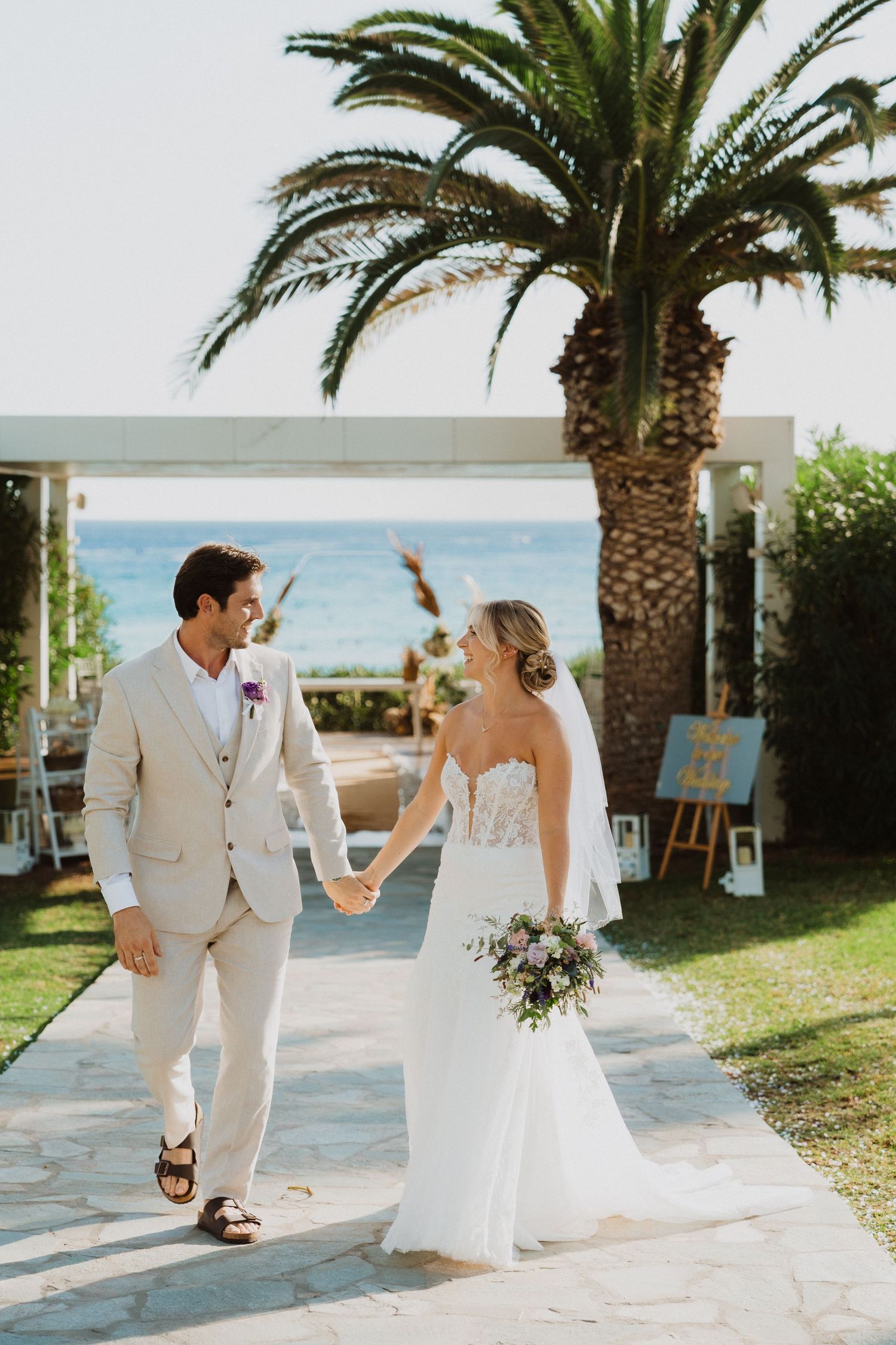 A beachside wedding celebration with a couple walking hand in hand under a palm tree.