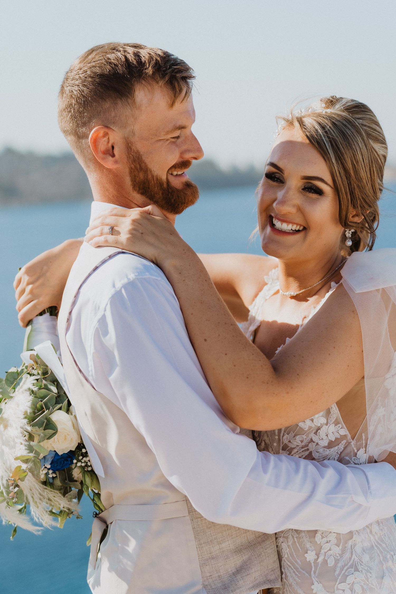 Romantic beach wedding couple embracing and laughing with ocean backdrop.