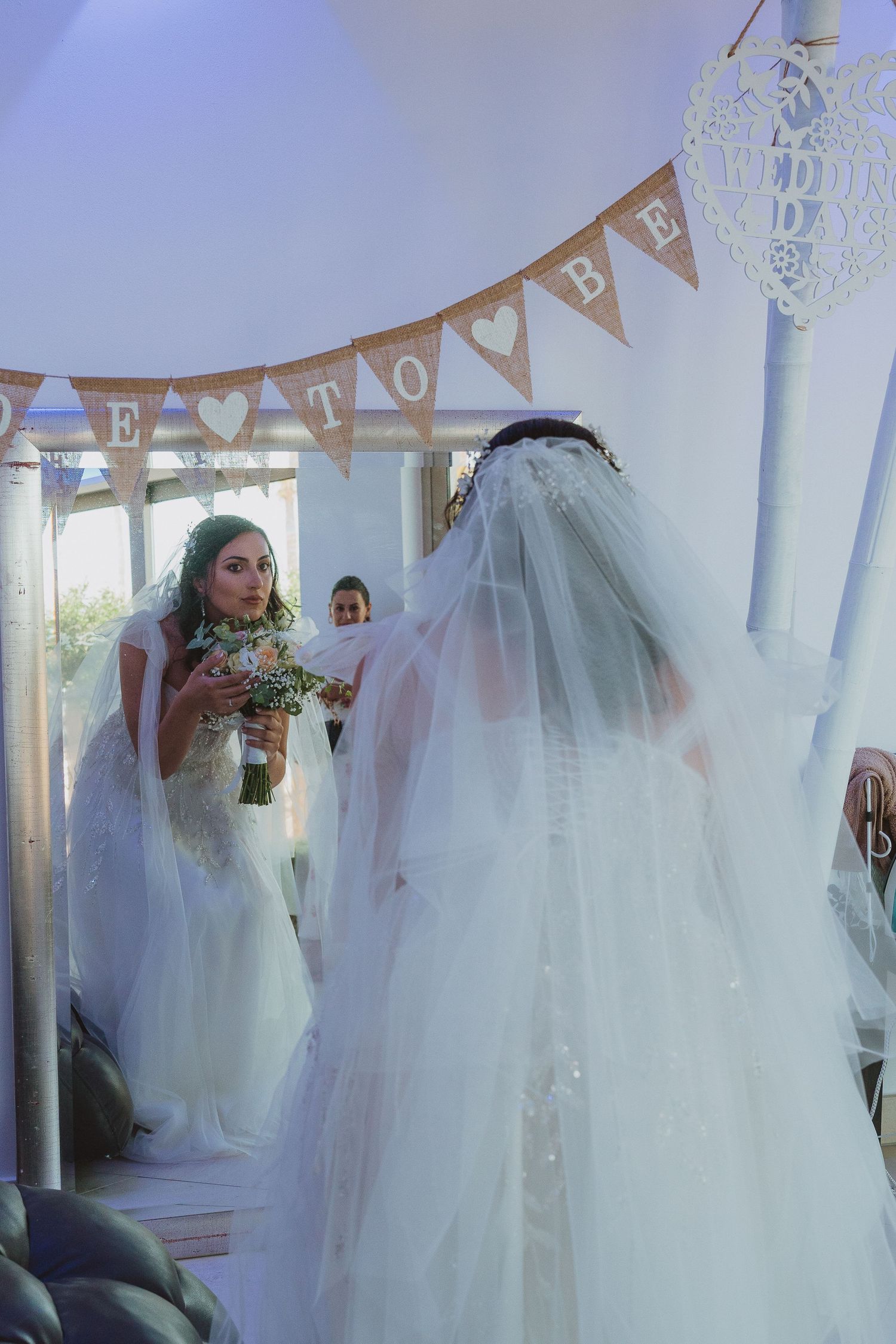 Two people in white wedding dresses stand together during a ceremony under a banner that says Love.