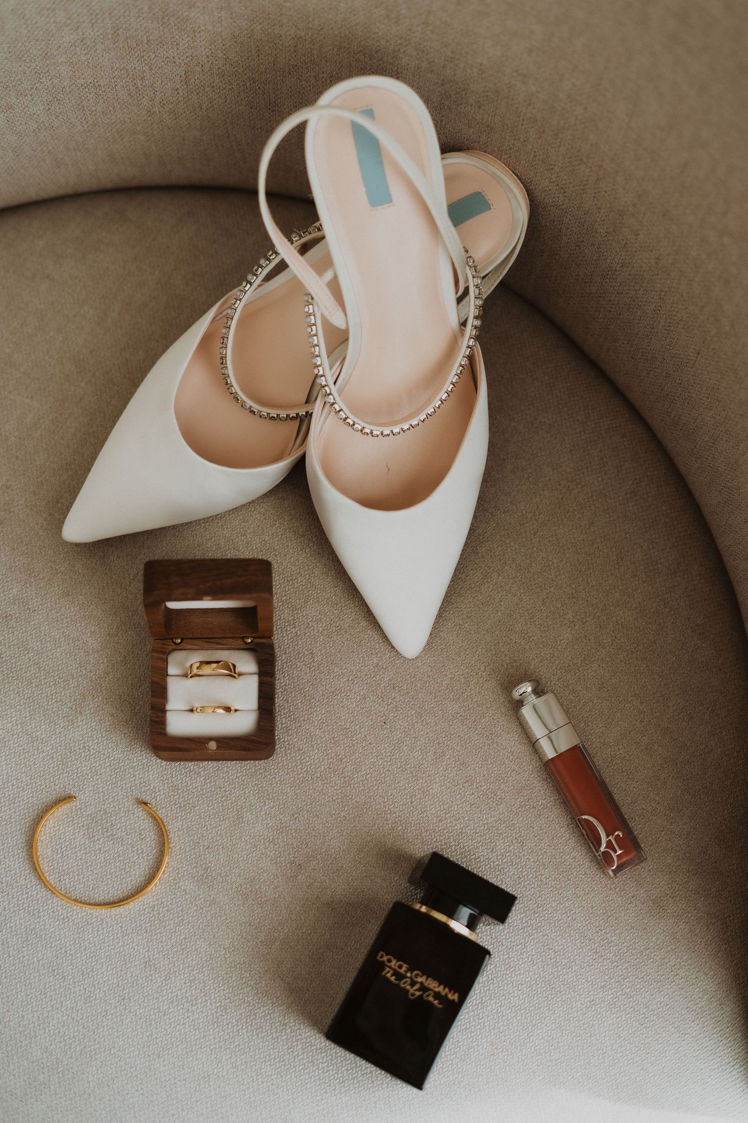 White bridal shoes with jewelry and accessories arranged on beige fabric.