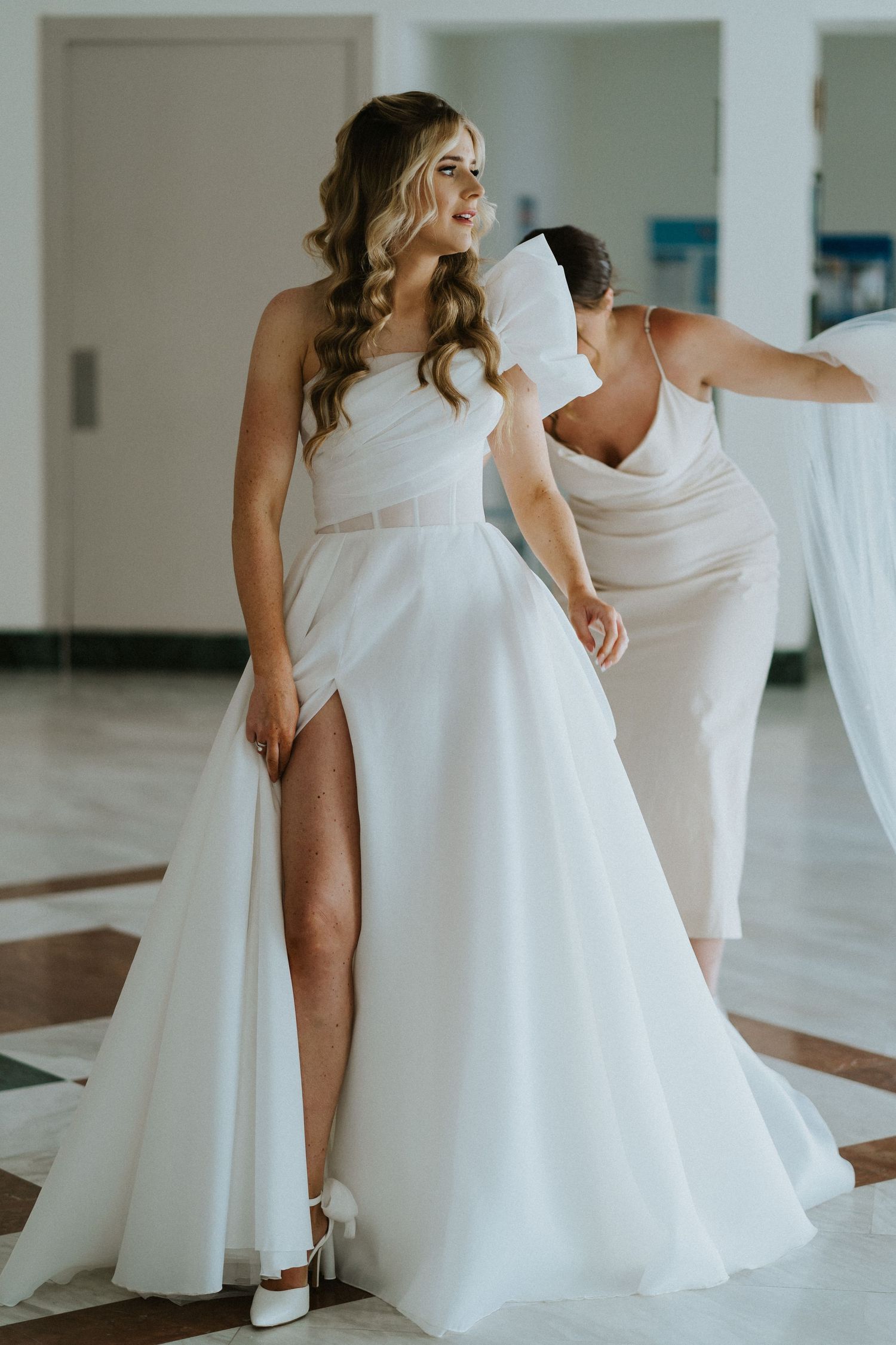 Elegant white wedding gown with a thigh-high slit and sweetheart neckline in a bright indoor setting.
