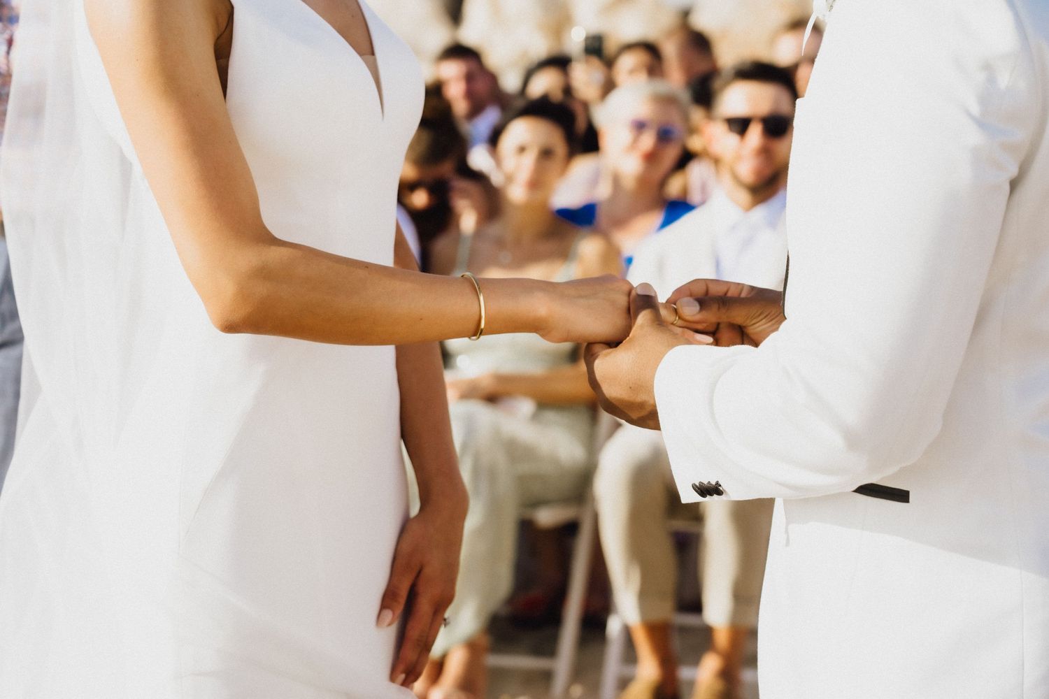 Close-up of wedding ceremony ring exchange with seated guests in background.