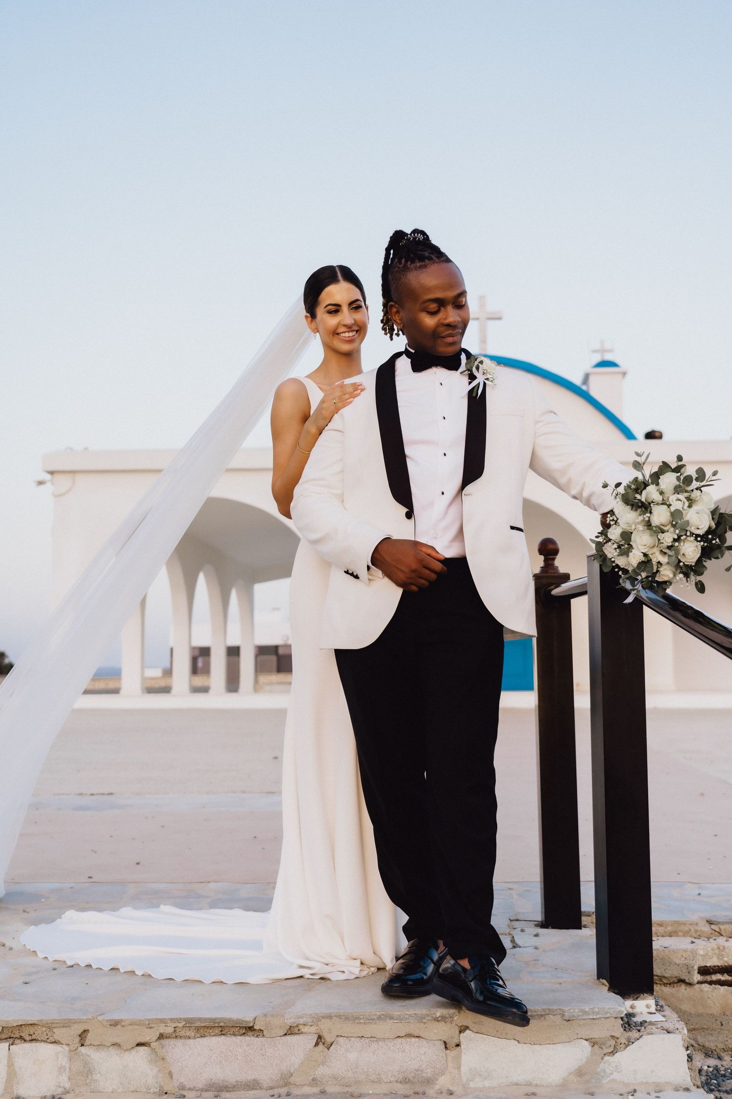 Wedding couple in classic white attire poses on Mediterranean steps.