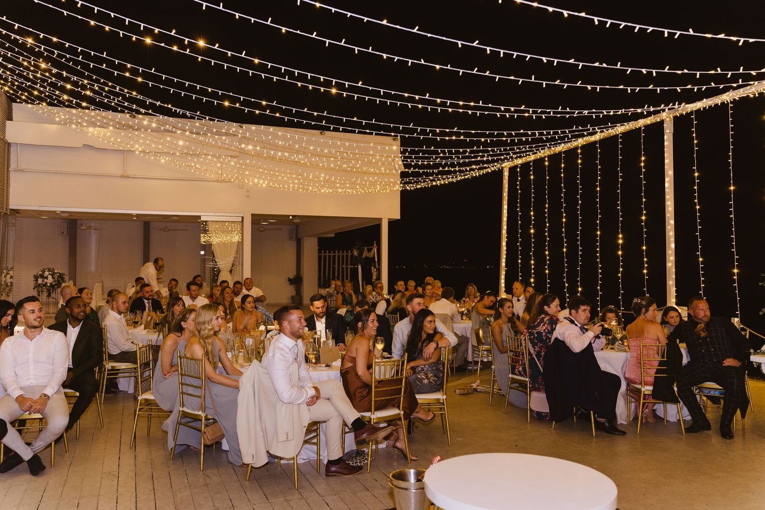 Wedding reception venue with string light ceiling and guests seated at round tables.