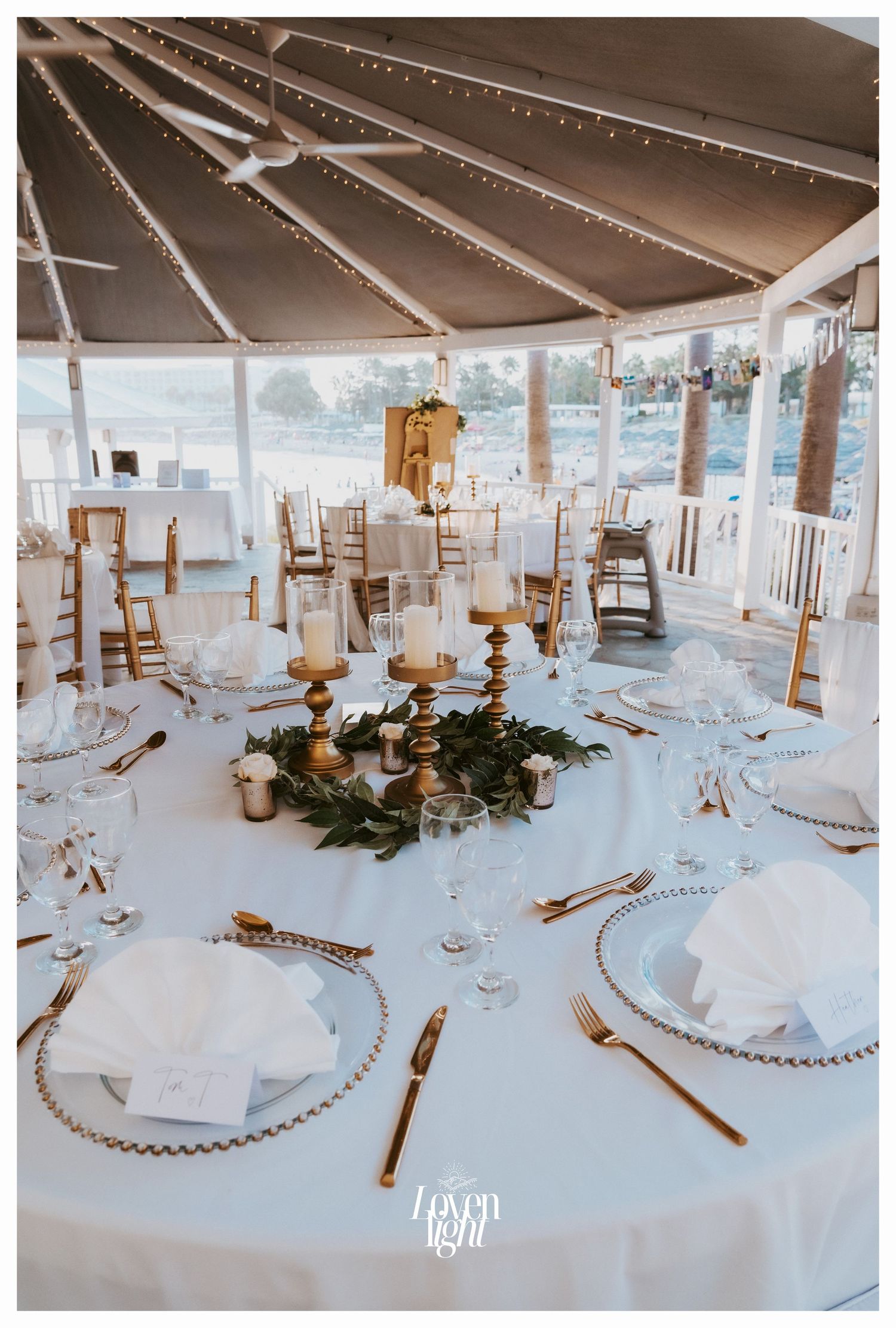 Elegant wedding table setting under tent with string lights and coastal view.