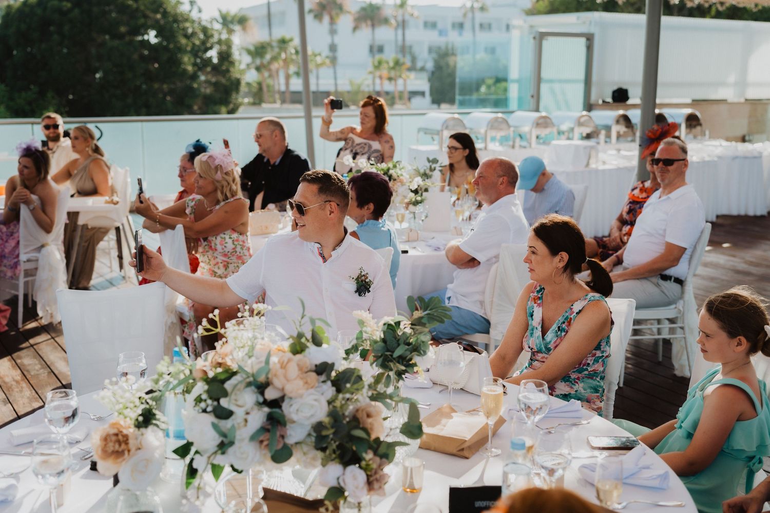 Wedding guests enjoy an elegant outdoor reception with floral centerpieces and string lights overlooking the ocean.