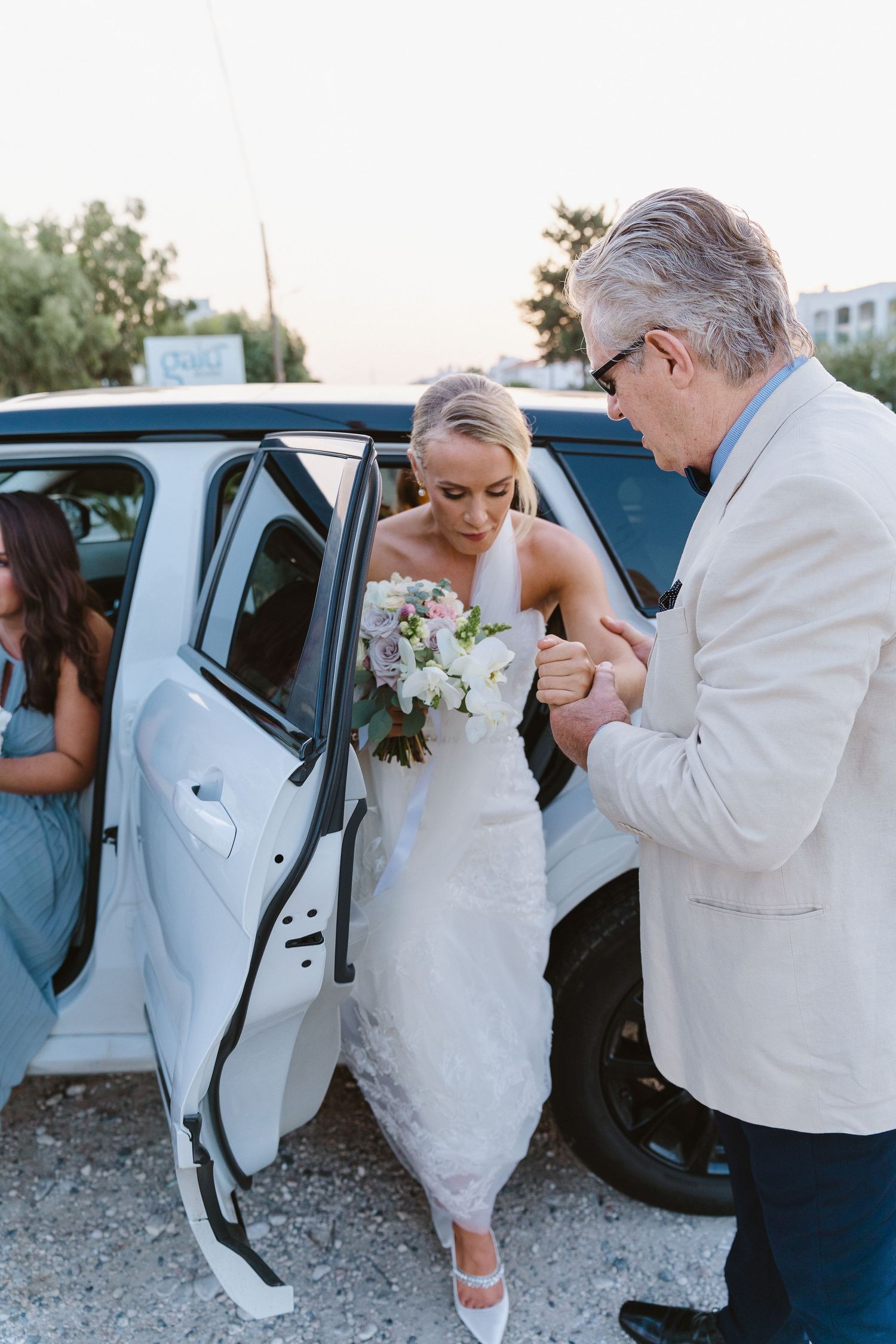 Elegant wedding arrival scene at a car with formal attire and floral bouquet.