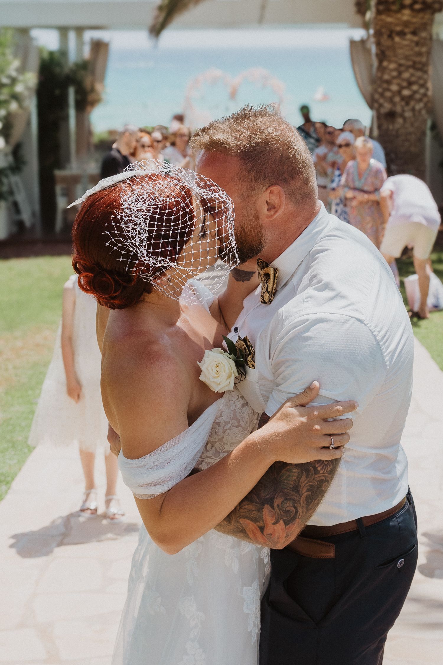 Intimate wedding kiss moment with guests celebrating in the background.