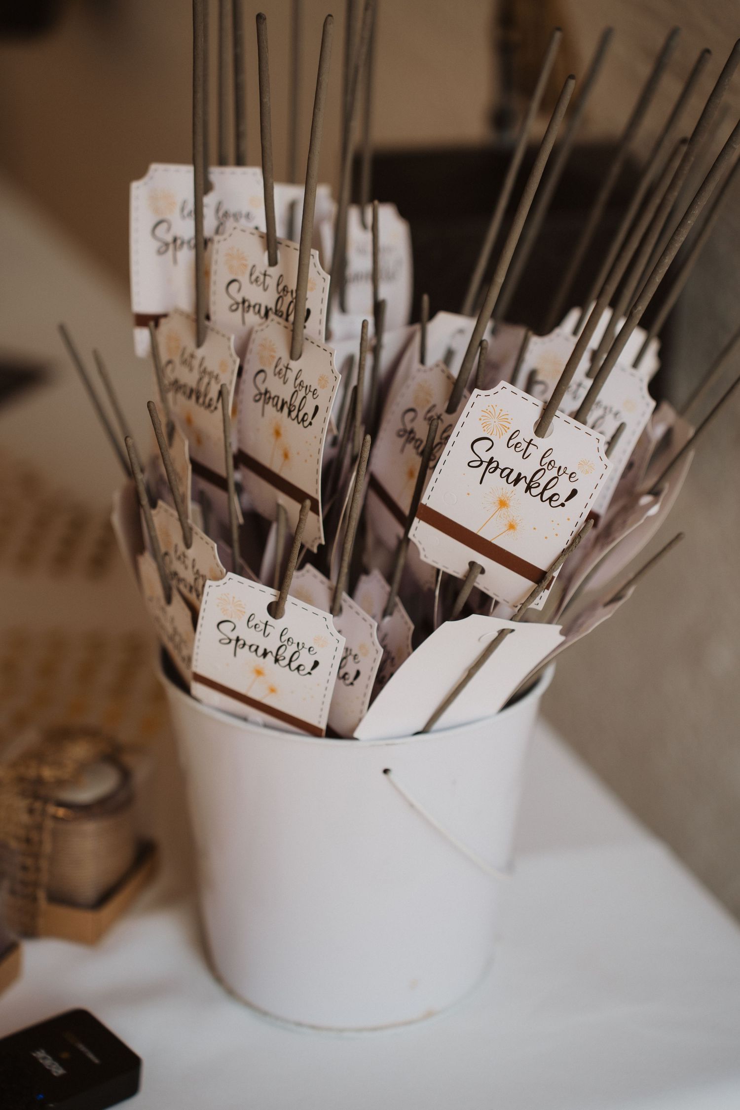 White bucket filled with sparklers tagged with Let Love Sparkle labels for a wedding send-off celebration.