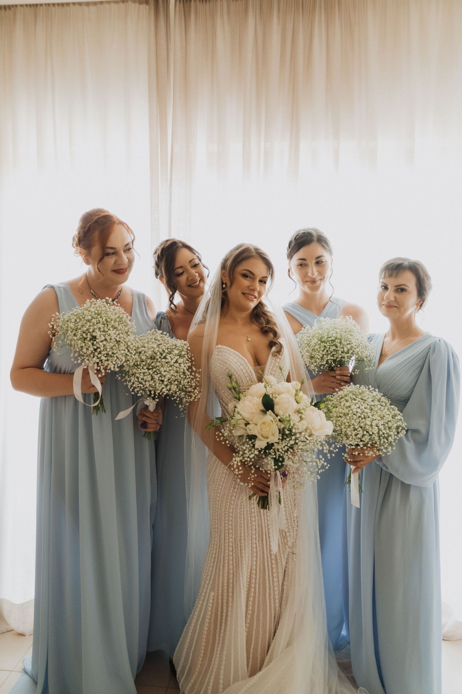 Bride in beaded gown with four bridesmaids in light blue dresses holding white floral bouquets.