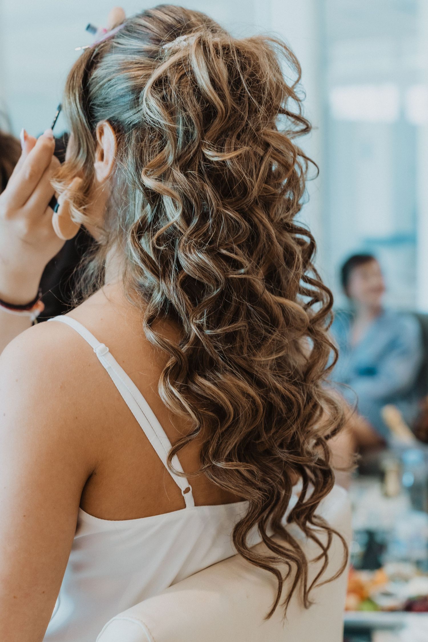 Bride with long curly highlighted hair being styled for her wedding day.