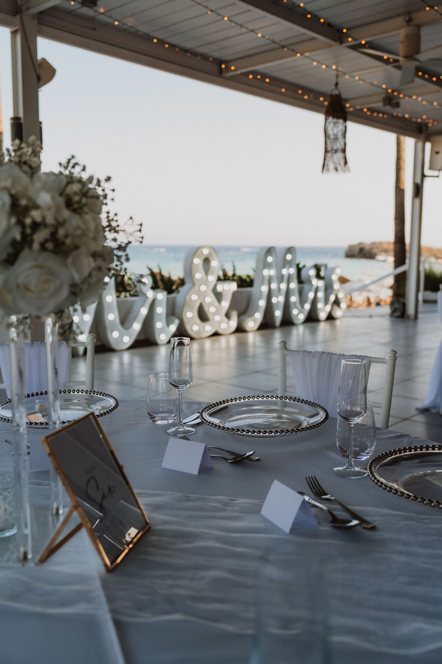 Coastal wedding reception table with Mr & Mrs marquee letters and place settings overlooking the ocean.