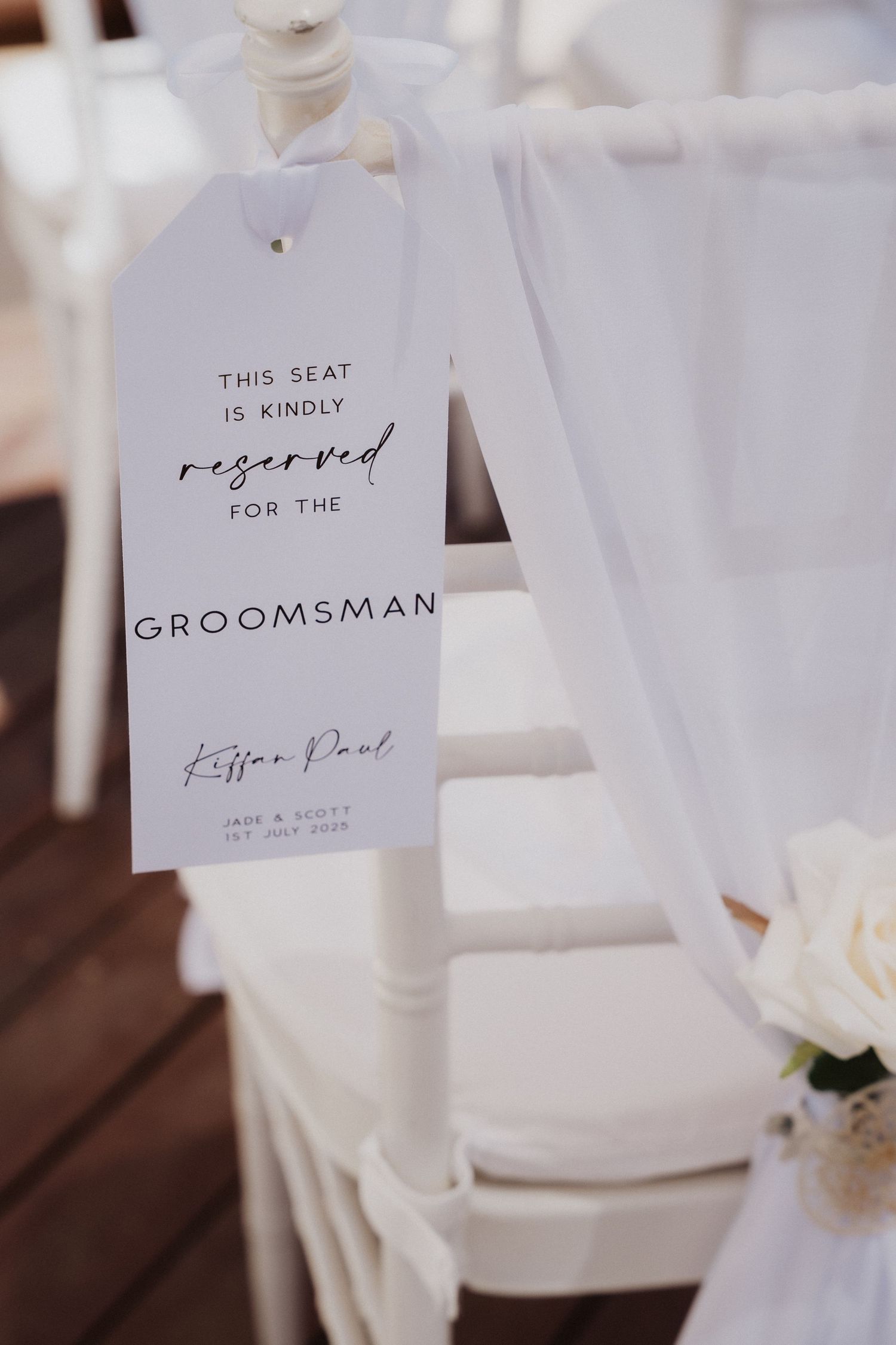 Elegant white reserved seating signs for groomsman displayed at wedding ceremony with delicate calligraphy text.