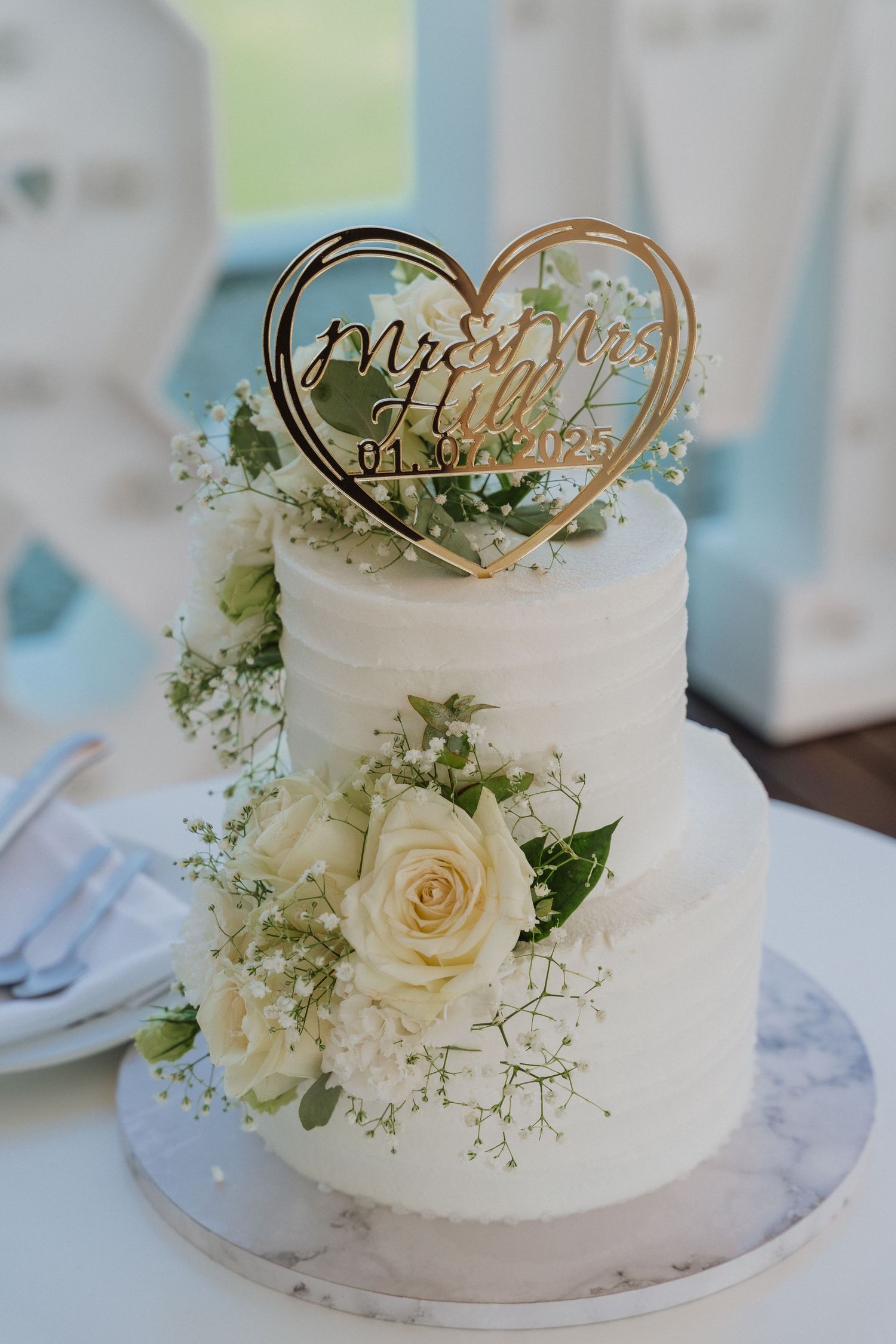 Elegant two-tier white wedding cake decorated with fresh roses, baby's breath and a gold Mr & Mrs heart topper.