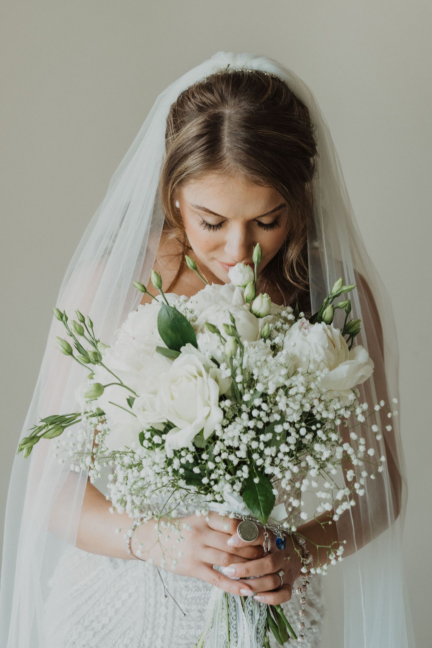 Bride in white veil smelling elegant bouquet of white roses and baby's breath.