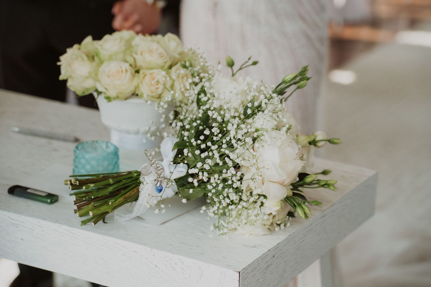 Bridal bouquets of white roses and baby's breath arranged on white wooden table.