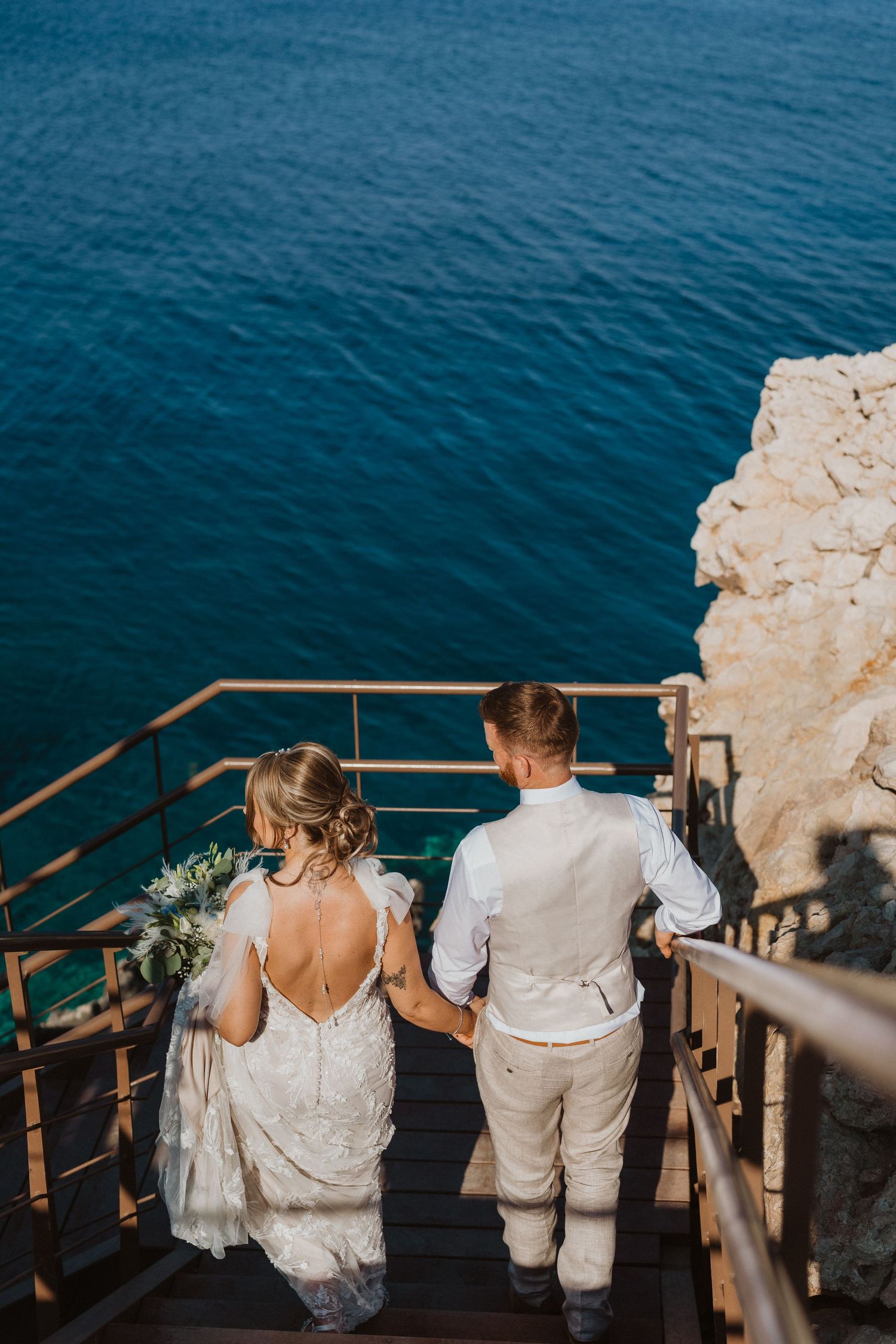 Couple sitting on wooden steps overlooking deep blue ocean waters.