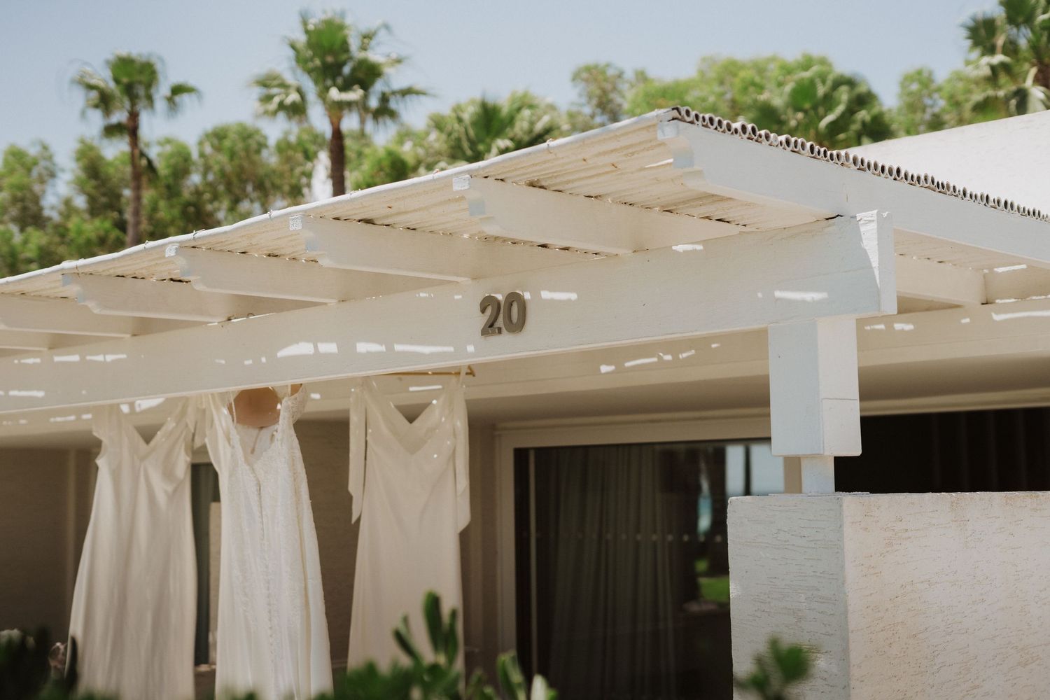White wedding dresses hanging under a pergola at a tropical resort venue.