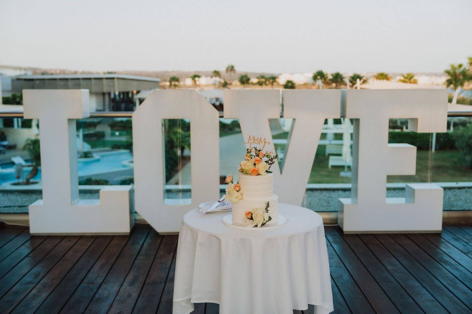 White wedding reception tables set up on an outdoor deck with ocean views.