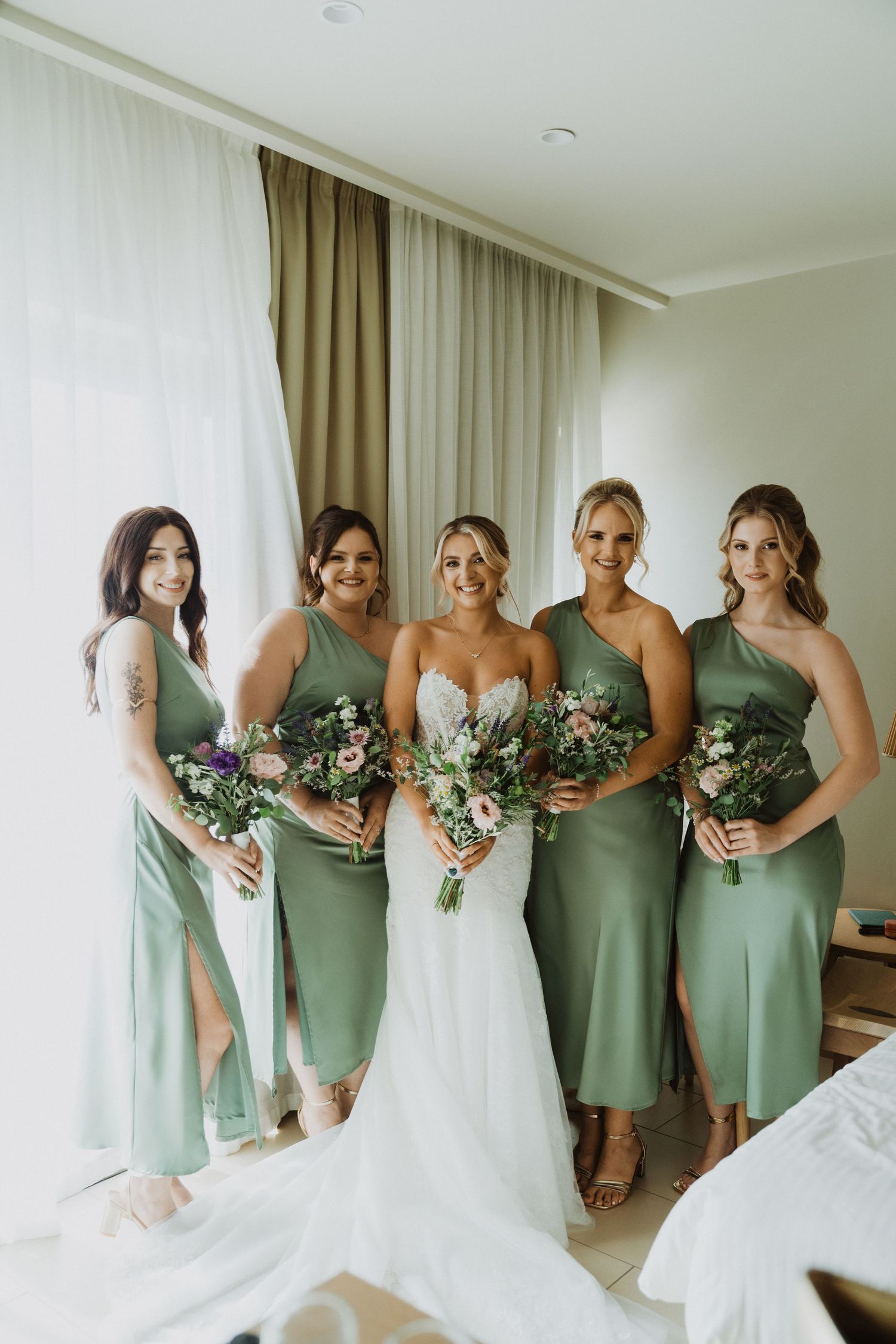 Elegant bridal party photo with sage green bridesmaid dresses and white wedding gown.