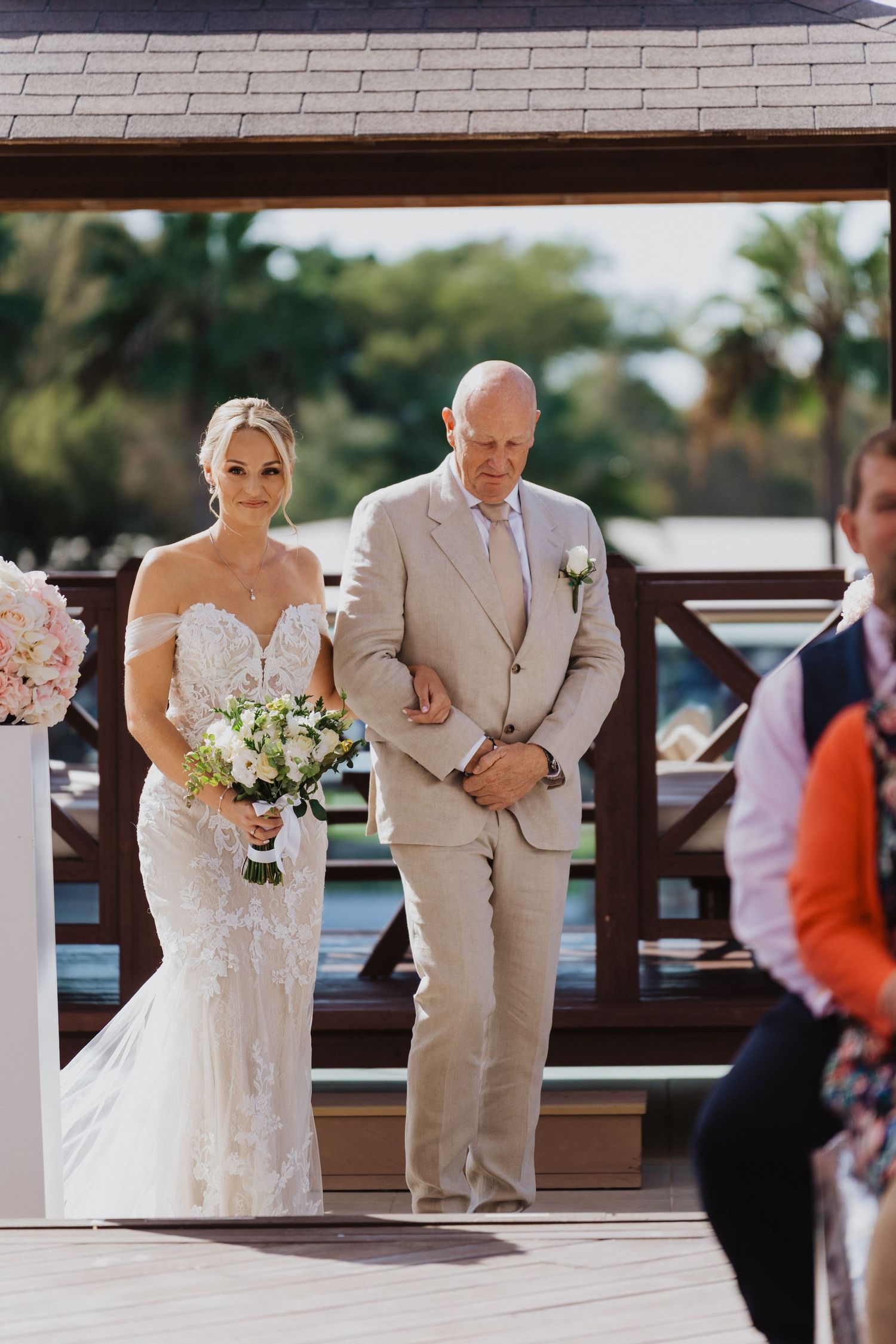 Wedding processional on a wooden deck with white columns and covered pavilion.