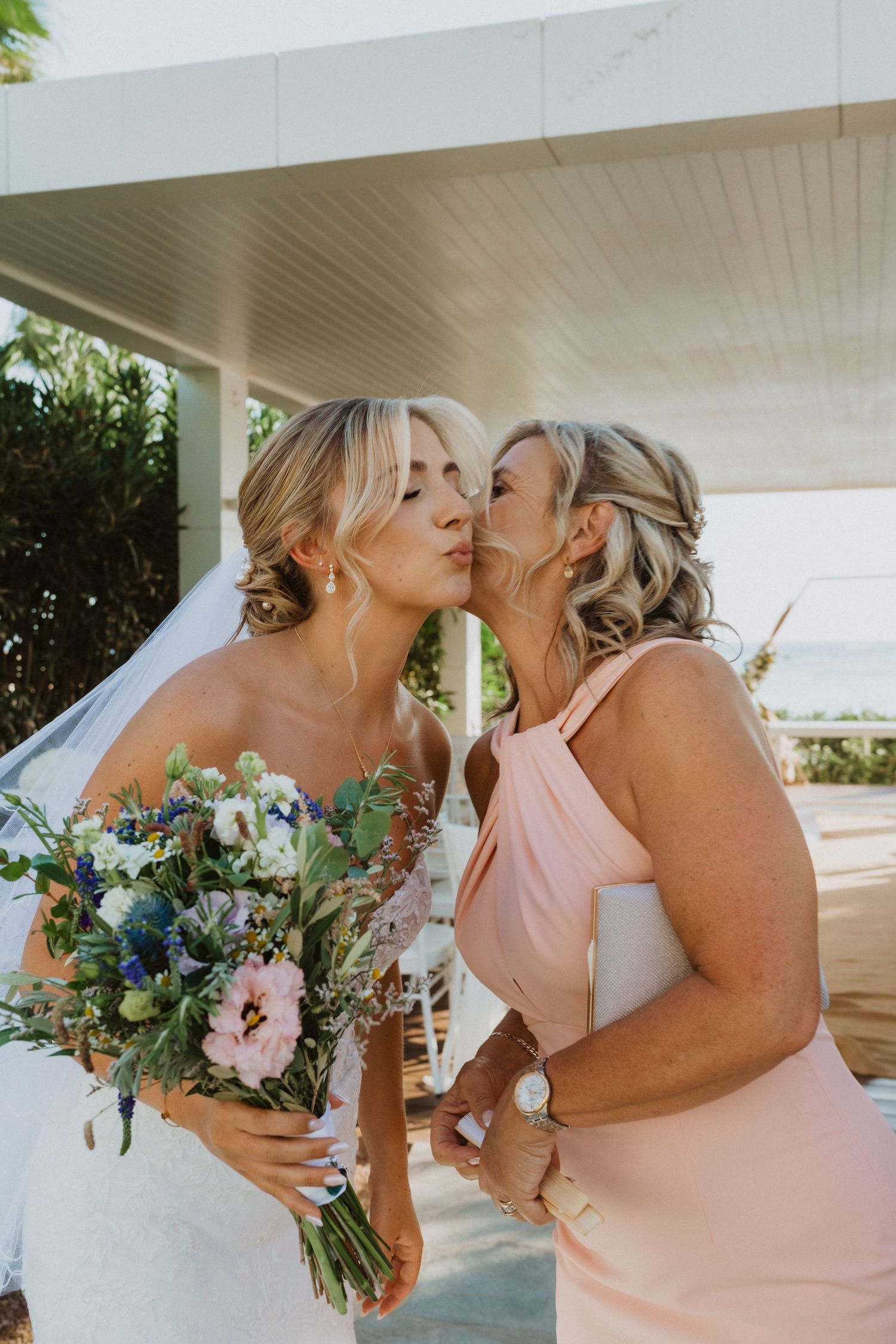 Wedding party members share intimate moments while holding floral bouquets.